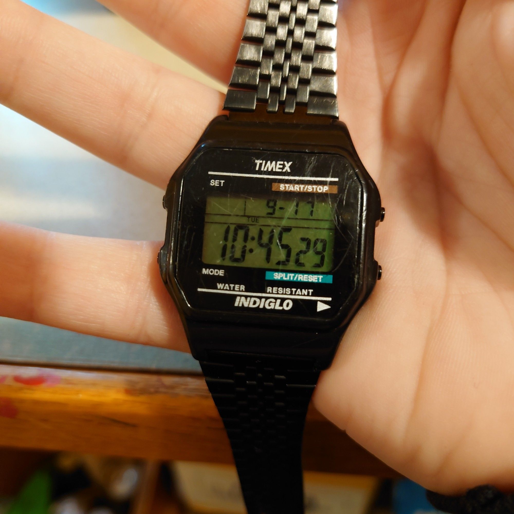 An old Timex T80 watch. It's well worn, the black armband is partially worn away to the bare metal beneath. The face of the watch is also scratched up.