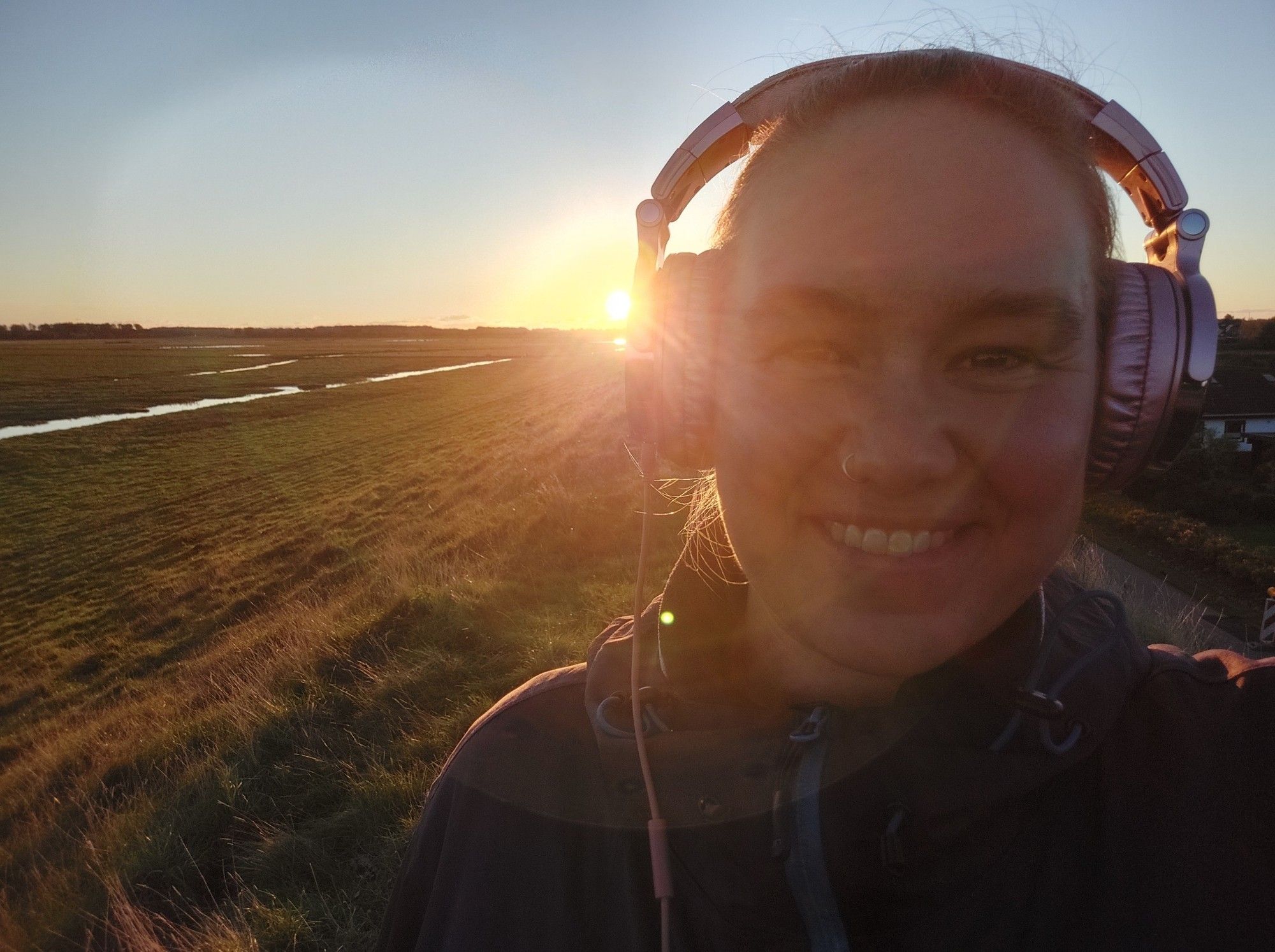 Selfie mit rosa Kopfhörern, hinter denen das goldene Licht der untergehenden Sonne hervorblitzt