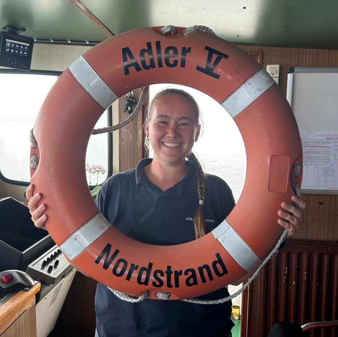 Auf der Brücke eines Schiffes. Ich halte einen orangen Rettungsring hoch und schaue und grinse durch die Öffnung hindurch in dir Kamera. Auf dem Ring steht: "Adler V - Nordstrand"
