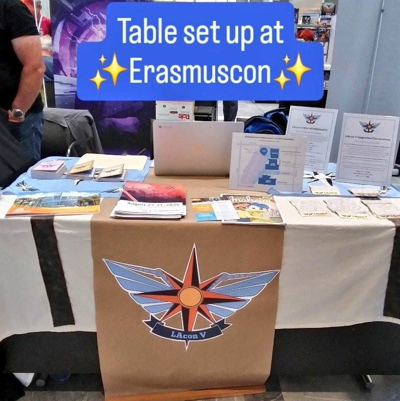 LA in 2026 table set up with branded tablecloth, freebies on table, signs describing how you can support the bid, and text above the scene reading table set up at Erasmuscon.