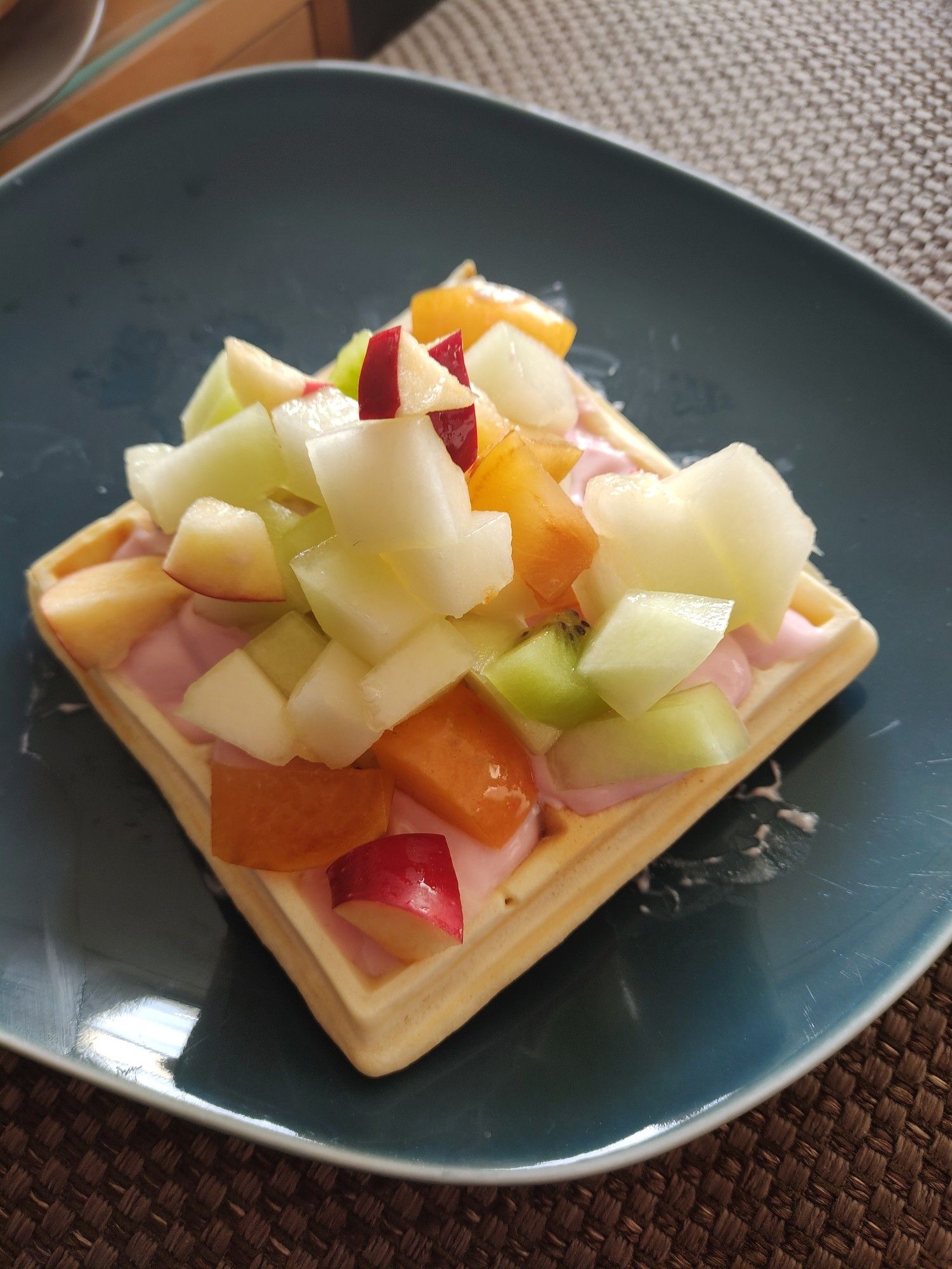 Eine Belgische Waffel mit Erdbeerjoghurt und Obstsalat auf einem blauen Teller