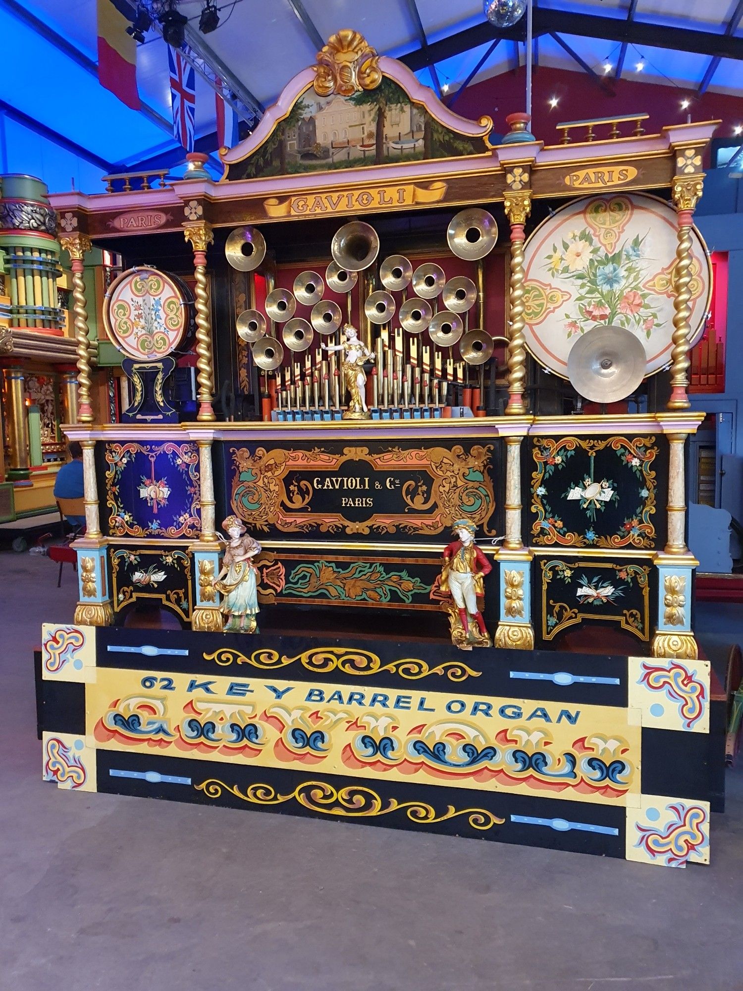 A Gavioli 62 key barrel organ with black and gold decoration, exposed organ pipes, a male and female figurine by the base and another figuring by the central horn panel