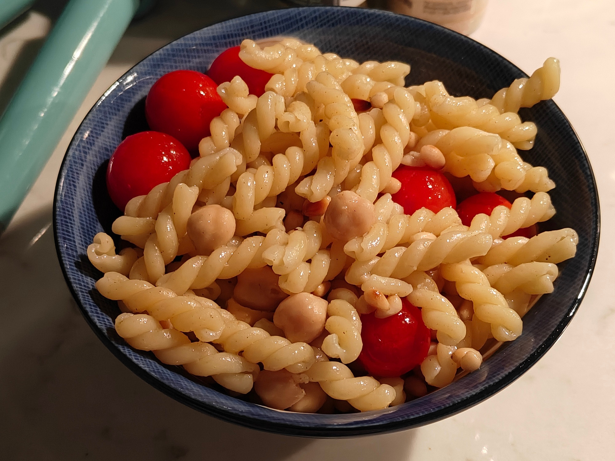 a bowl of spiral pasta with tomatoes, chickpeas, and pine nuts. it is seasoned with olive oil, pepper, sage, and garlic