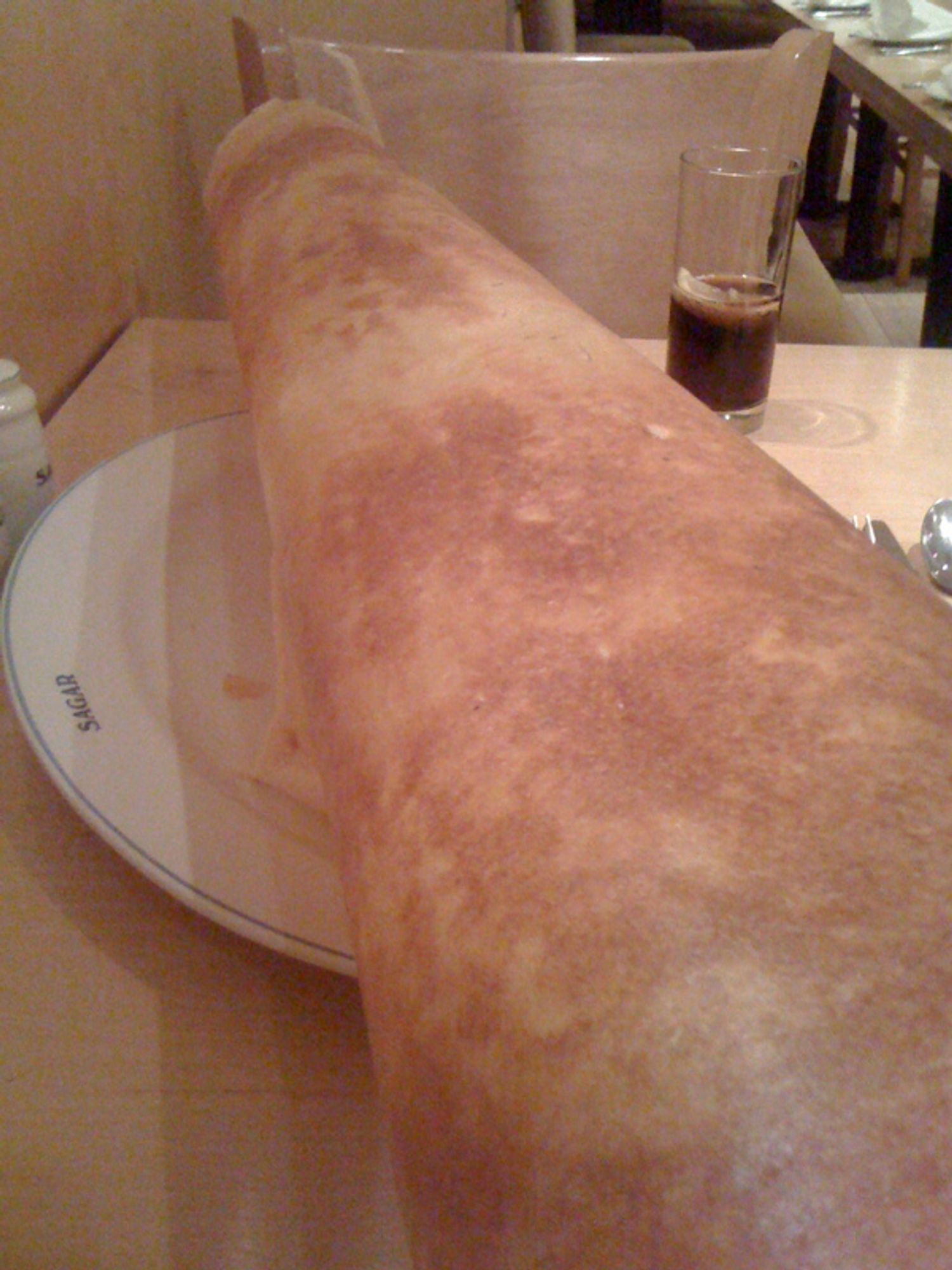 A paper thin, but gigantic dosa. So big it is extended many inches beyond the dinner plate it is sitting on.