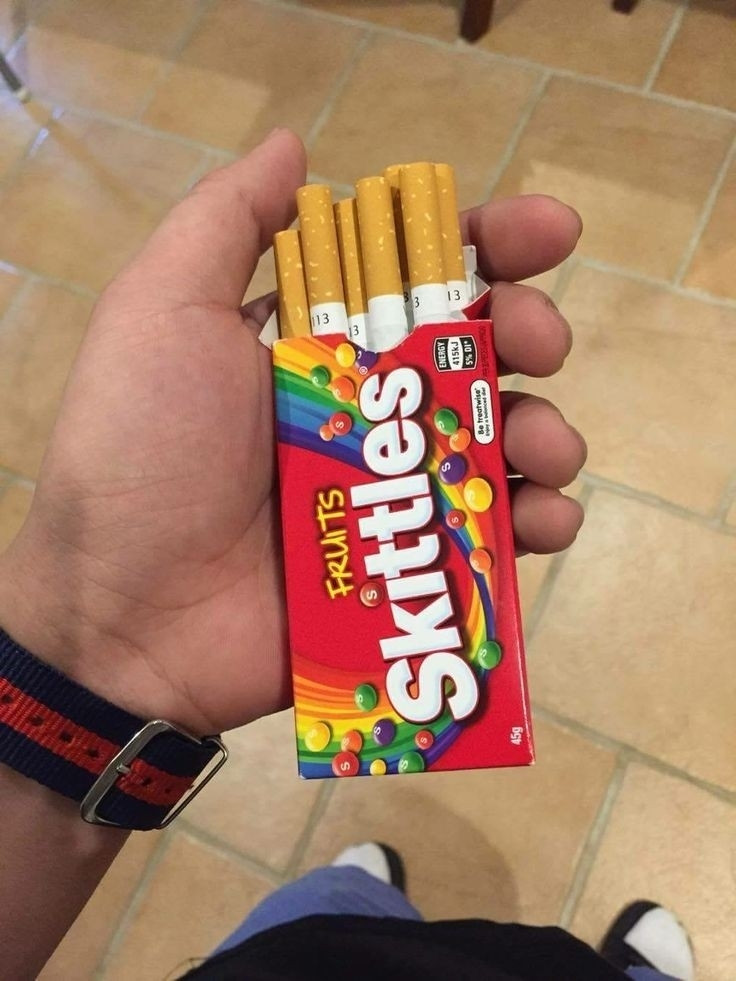 Hand holding Skittles package that actually has cigarettes in it.