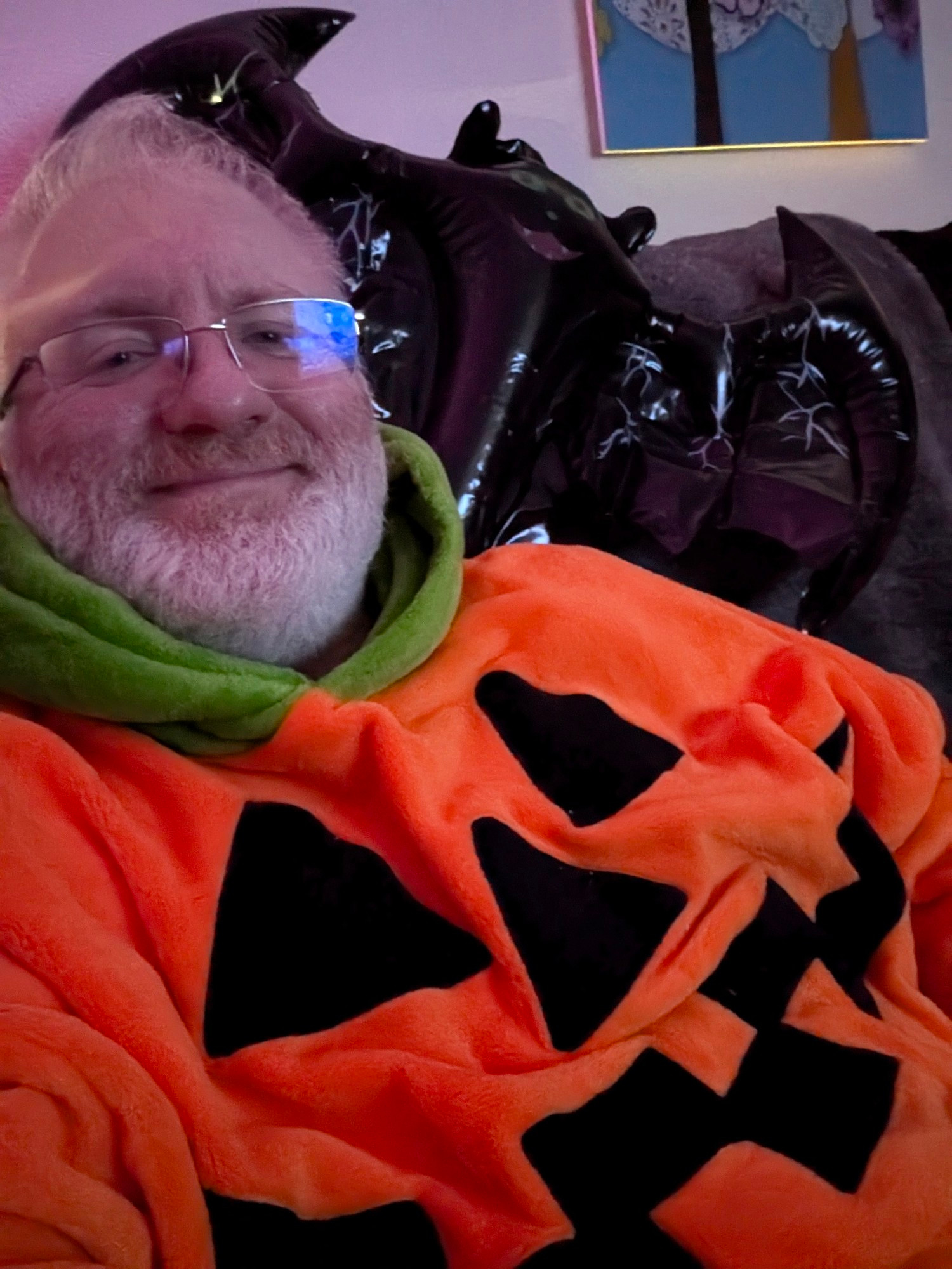 Man reclined. Dressed in a pumpkin hoodie with an inflatable bat on his shoulder signalling the start of spooky season.