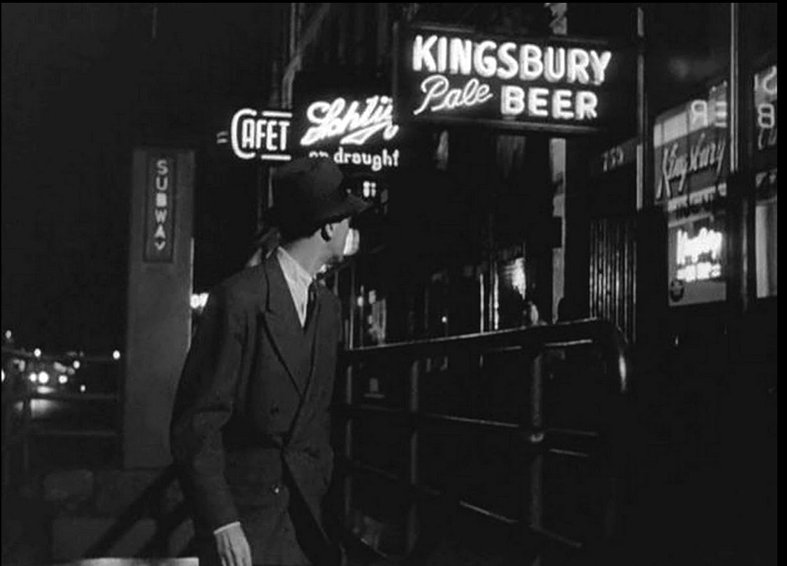 an image of the protagonist, walking the city street at night, looking backwards at a neon beer sigh that reads 'kingsbury pale beer', a sign for the subway behind him, he wears a fedora hat and a suit