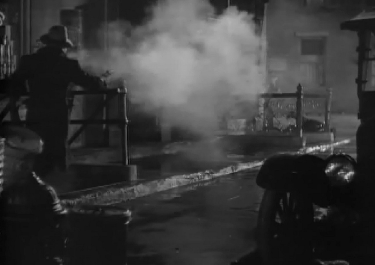 an image from the movie, it is a black and white film, a man in the streets, a gust of steamy smoke pouring out, a very noir-ish look to it