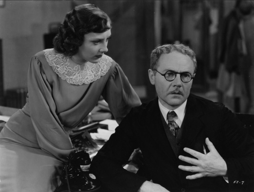 one of the male leads, holding his hand over his chest, his face looks exasperated, a woman on the left side leaning in to listen to him