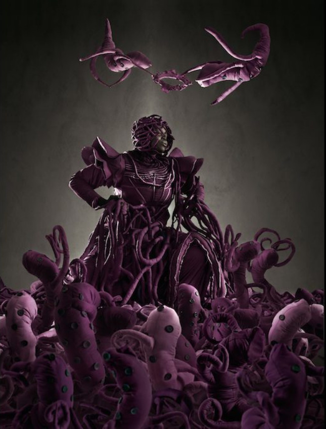 a photo of a woman in a purple dress, sitting, looking to the right, a black and white with grey toned background, purple organ-like tendrils on her, there are work-like creatures surrounding her, 2  worm-like creatures flying overhead of her