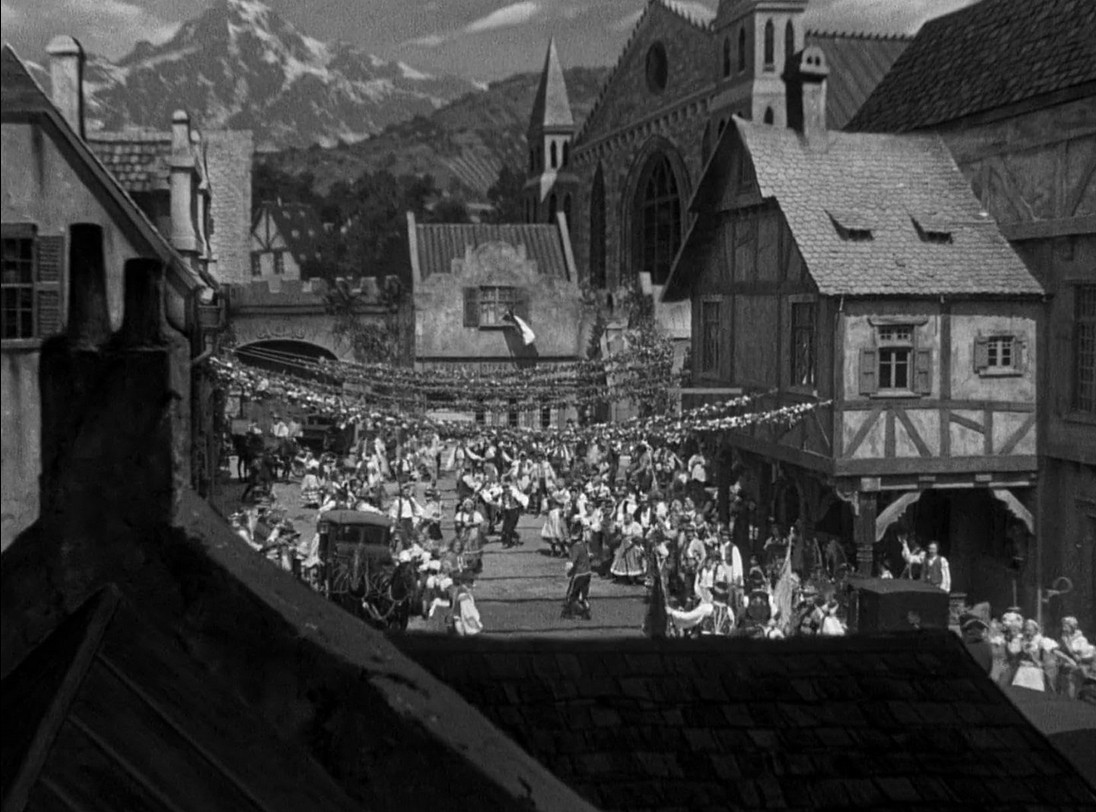 an image of an old timey european street scene, cute buildings, large mountains in the background 