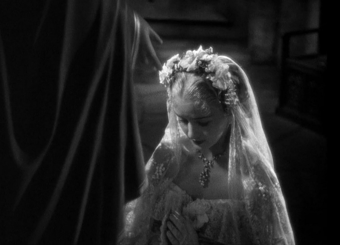 an image of a young woman as a bride, bowing with her hands together in prayer , a robed figure to the left of her, just his arm and cloak showing his hand outwards to her  