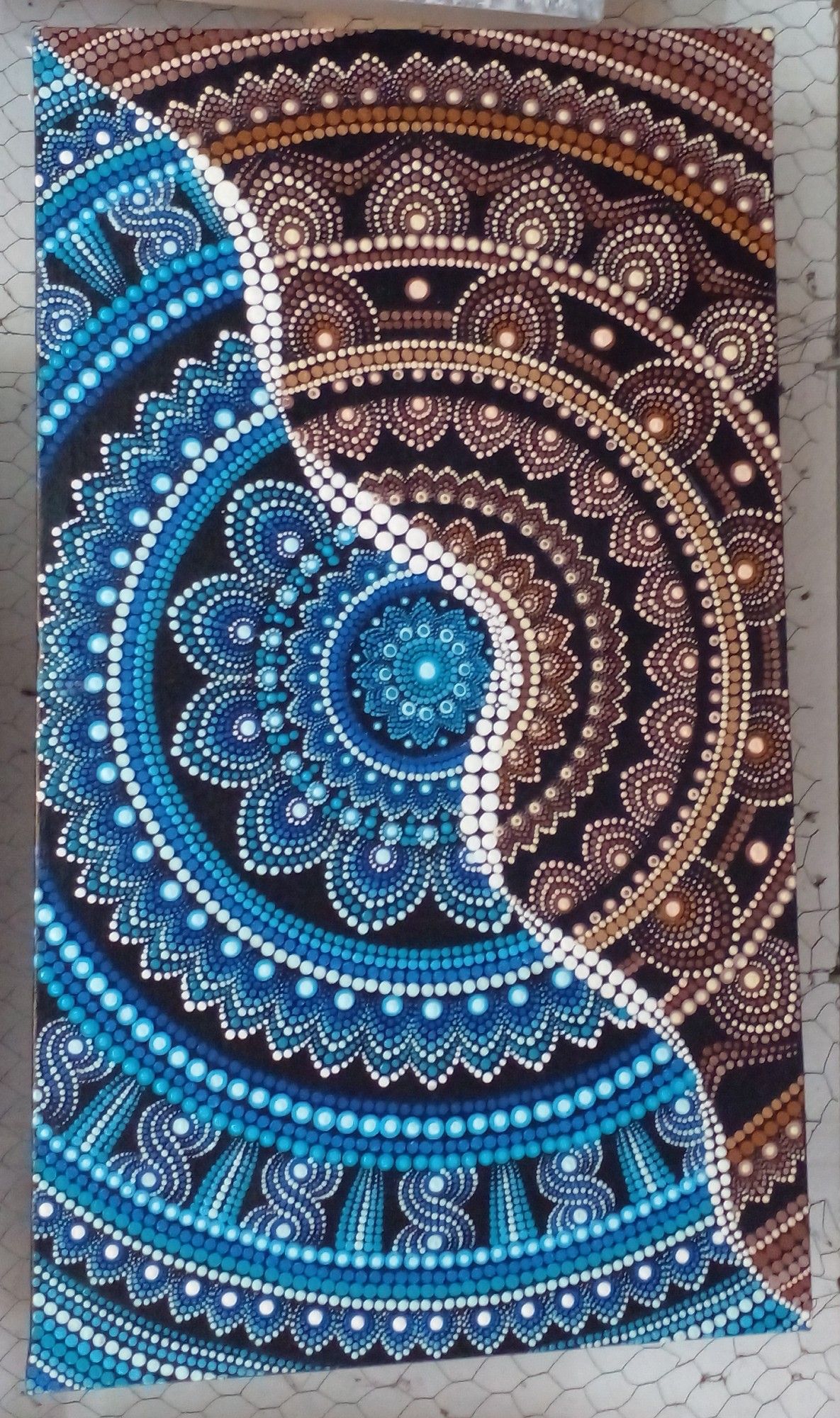 a mandala design, it is cropped at the sides, a wavey line going through diagonally, half is blue and black and white, the other half brown and black and white