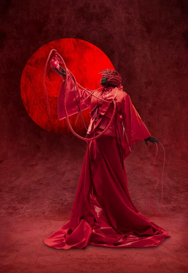 a photo of a woman in a red dress, in front of a red moon-like circle, raising up a heart in front of it, a red background