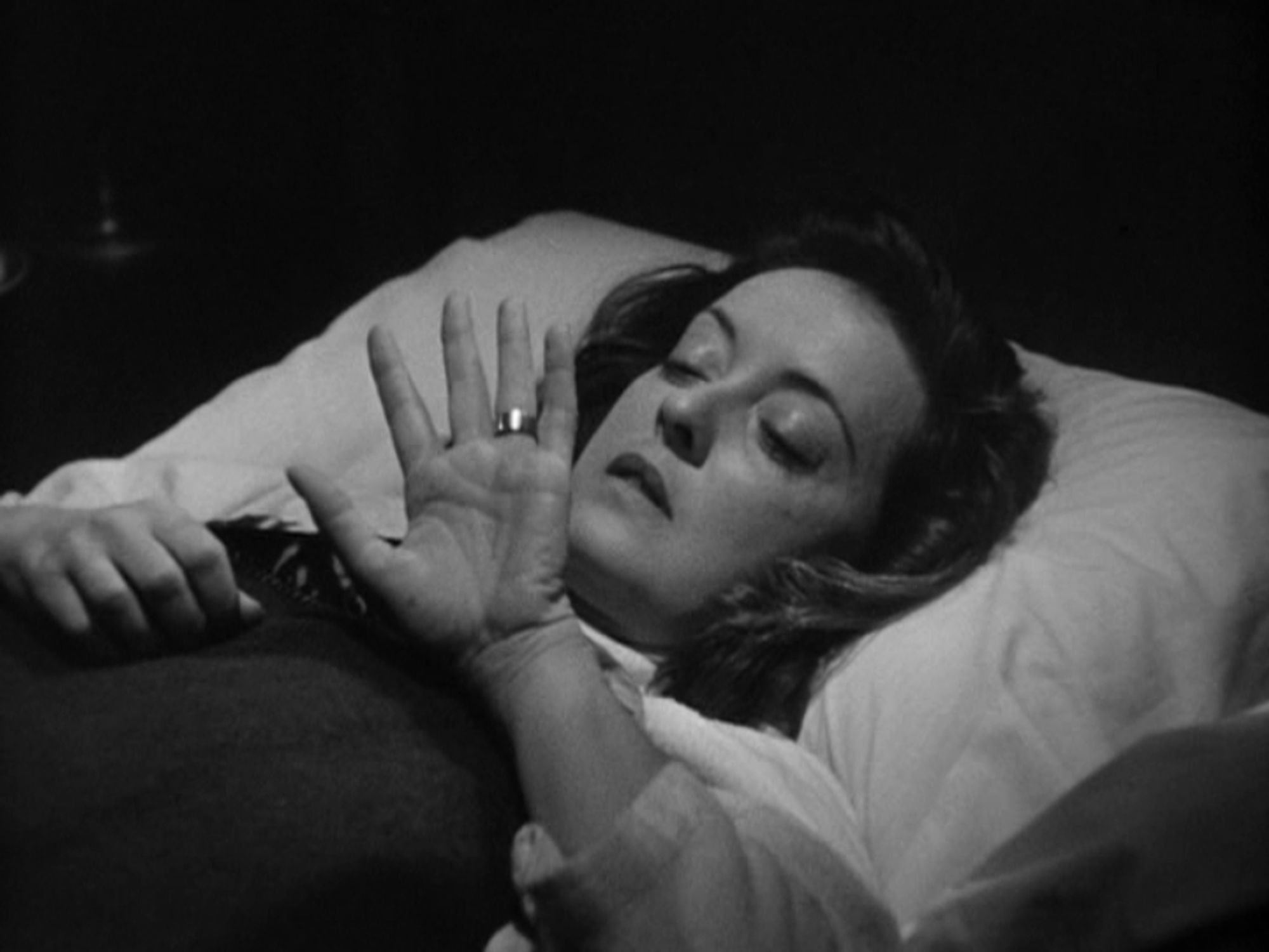 an image of bette davis in bed, looking at her dead twin sister's ring on her hand