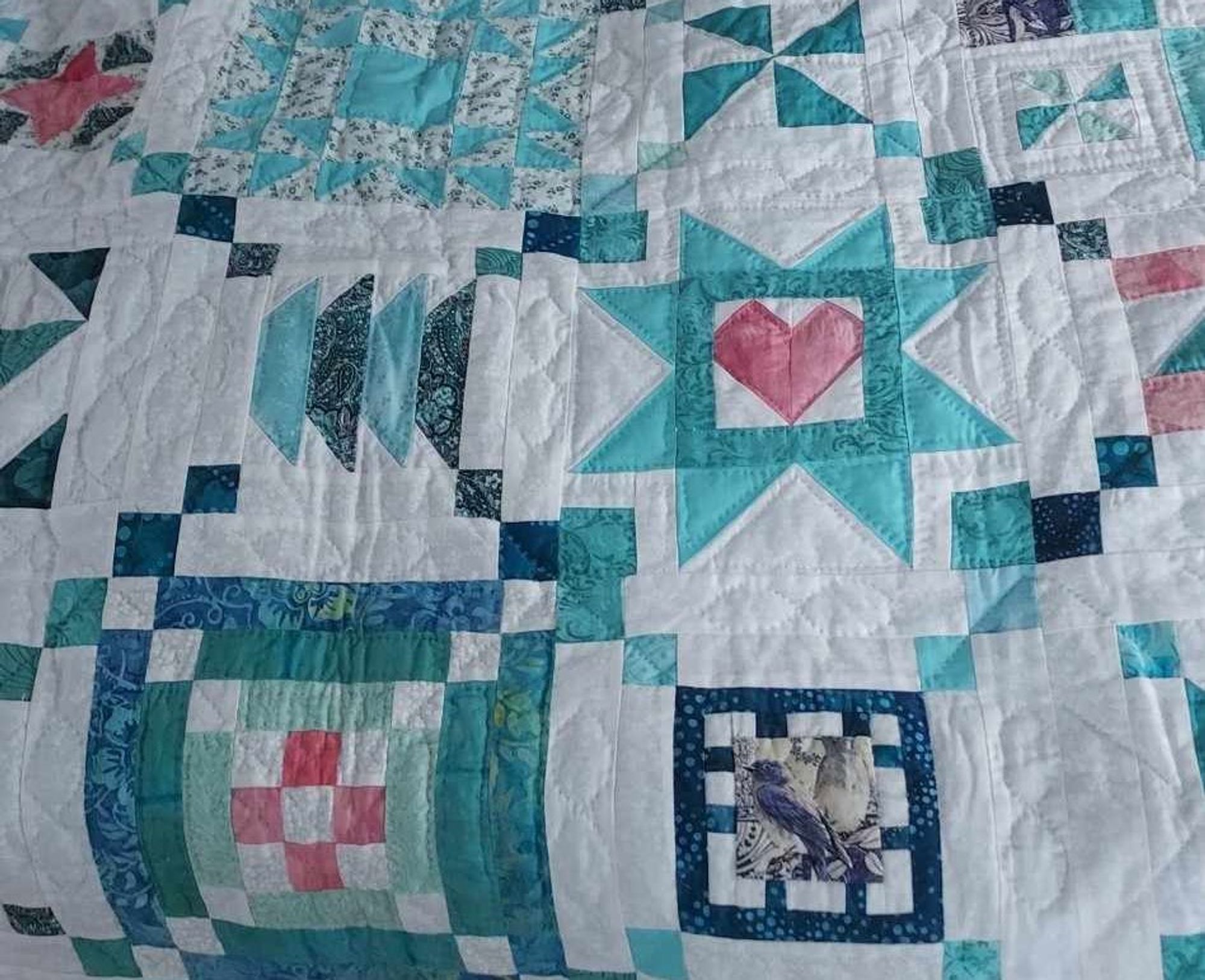 a close-up of a quilt, it is green and blue and light red pieces of fabric arranged into abstract geometric shapes on a white backing