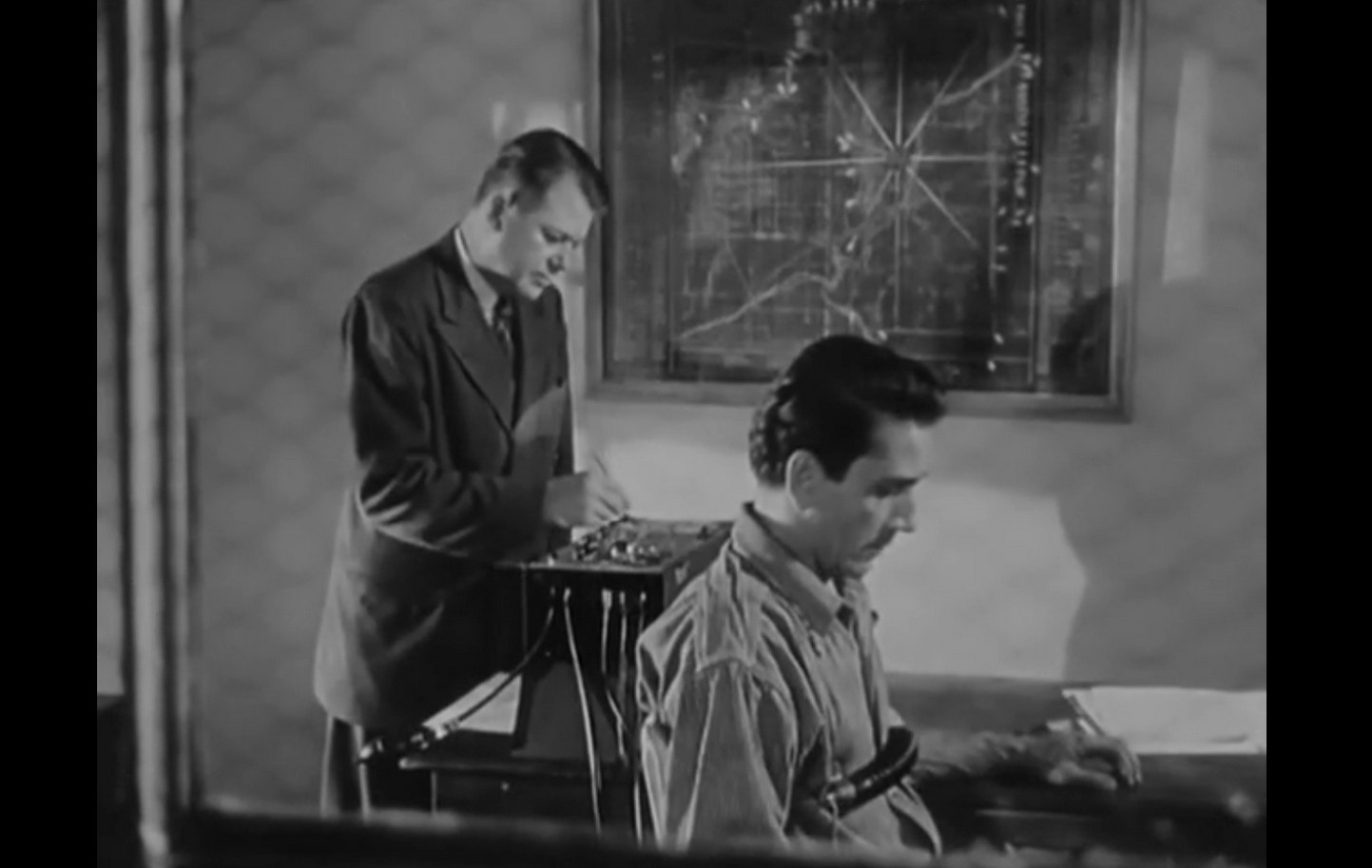 an image from the movie, through an observation window in a police station, a man is connected to a lie detector and questioned by a detective