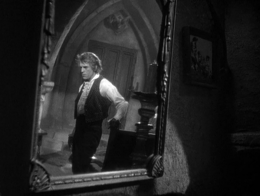 an image of boris karloff seen in a mirror in a room, an upset expression on his face 