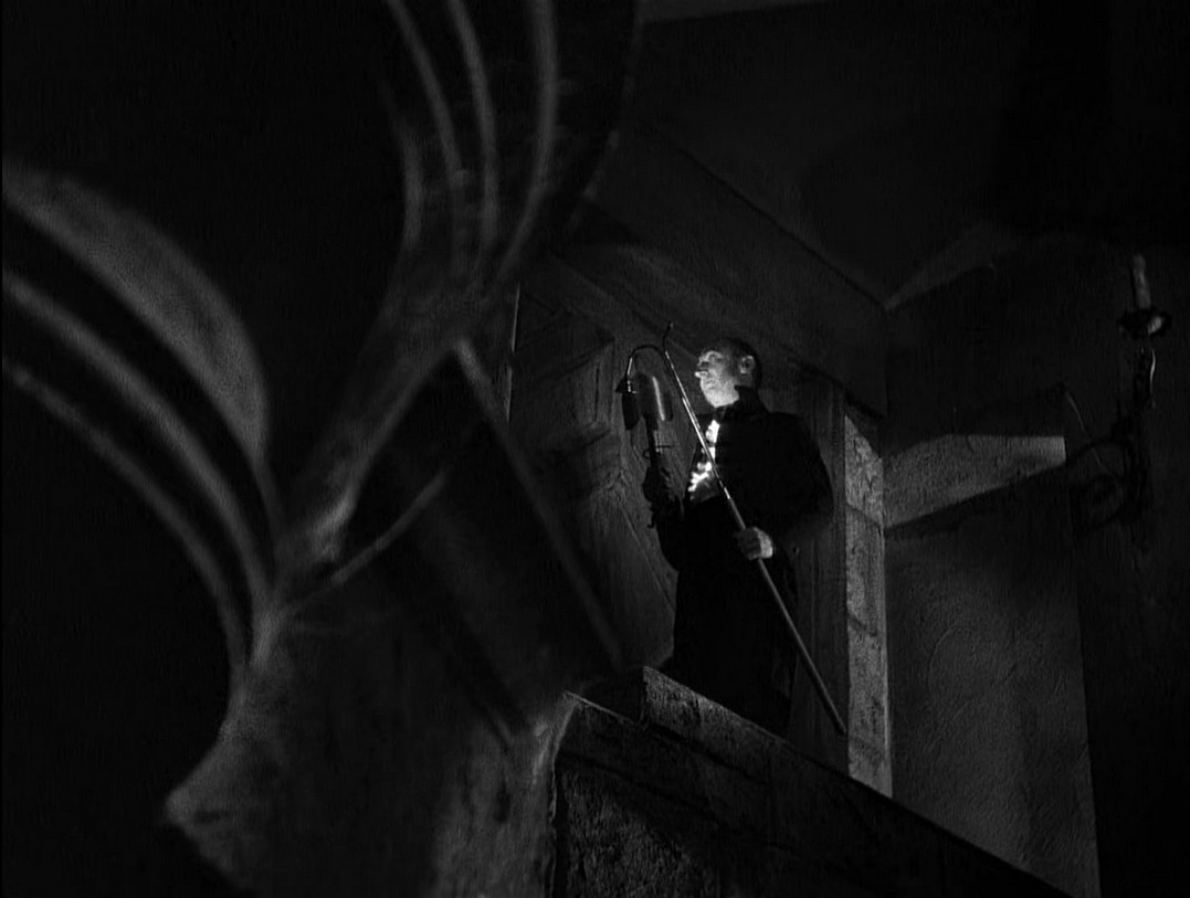 an image of a man walking up steps in a dark old manor, a lantern on a short thin metal pole in his hands 