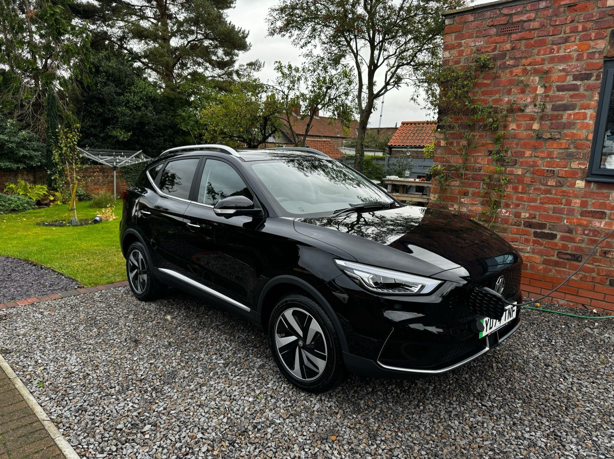 A new black shiny car is charging on a drive way.