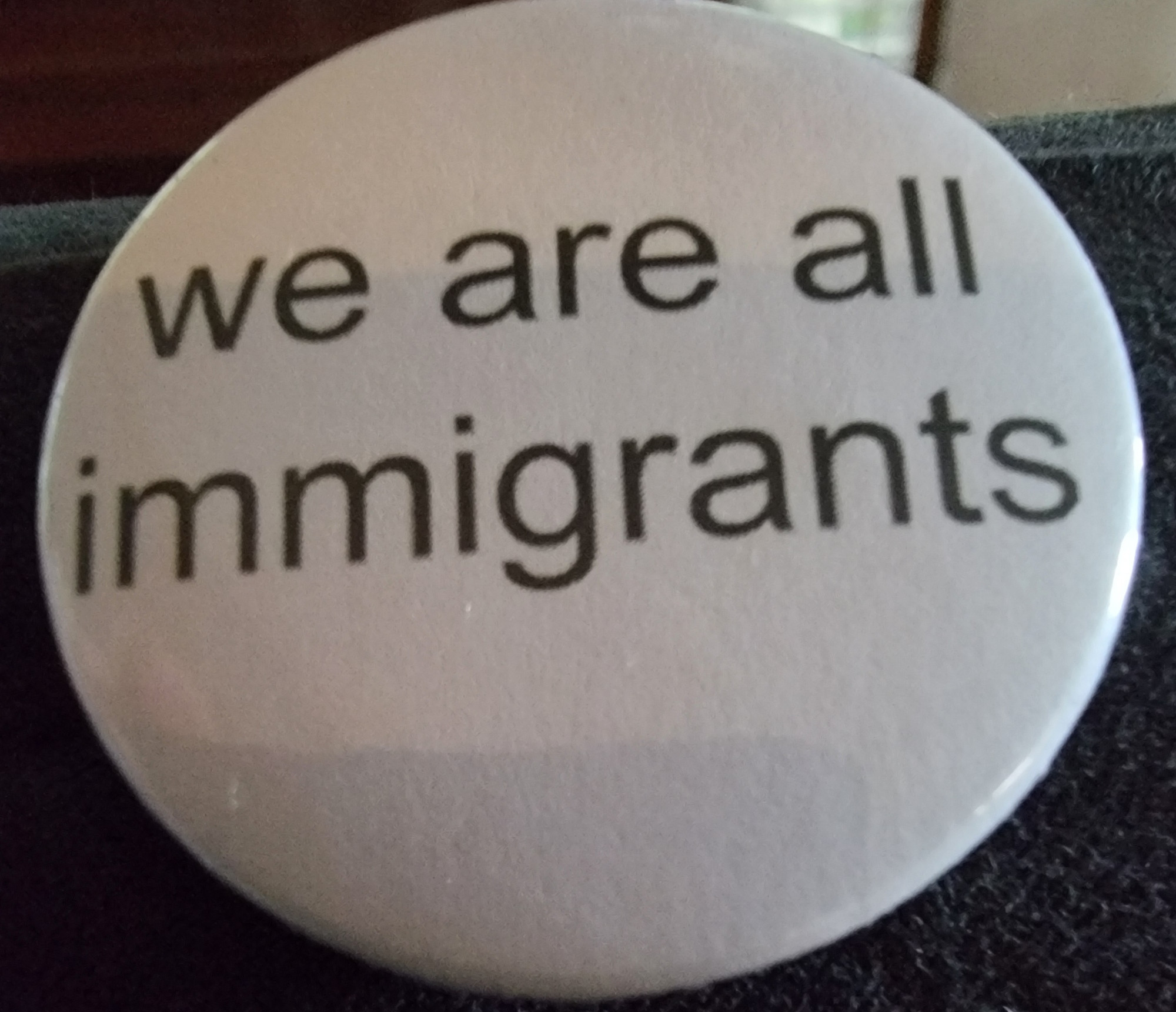 A white button with black printing that says "we are all immigrants." 