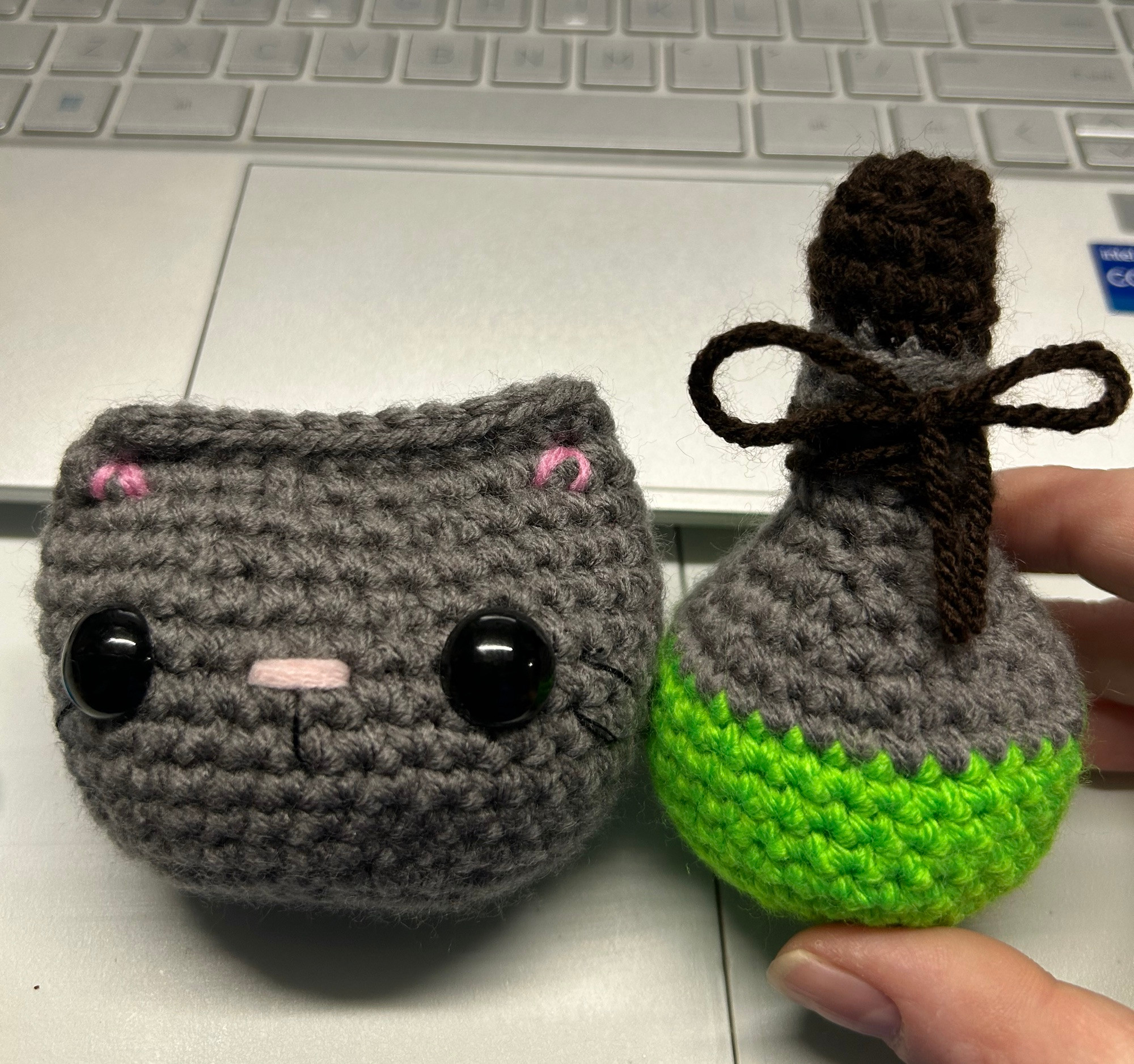 Photo of crocheted grey cat face and green and grey potion bottle with a brown bow