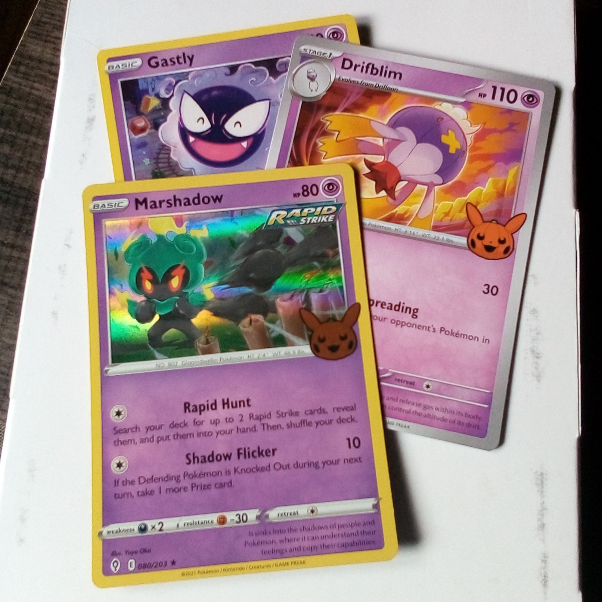 rapid strike marshadow (holographic), drifblim, and gastly TCG cards. the rapid strike set is focused on low-cost attacks. its counterpart set, single strike, focuses on KOs instead.