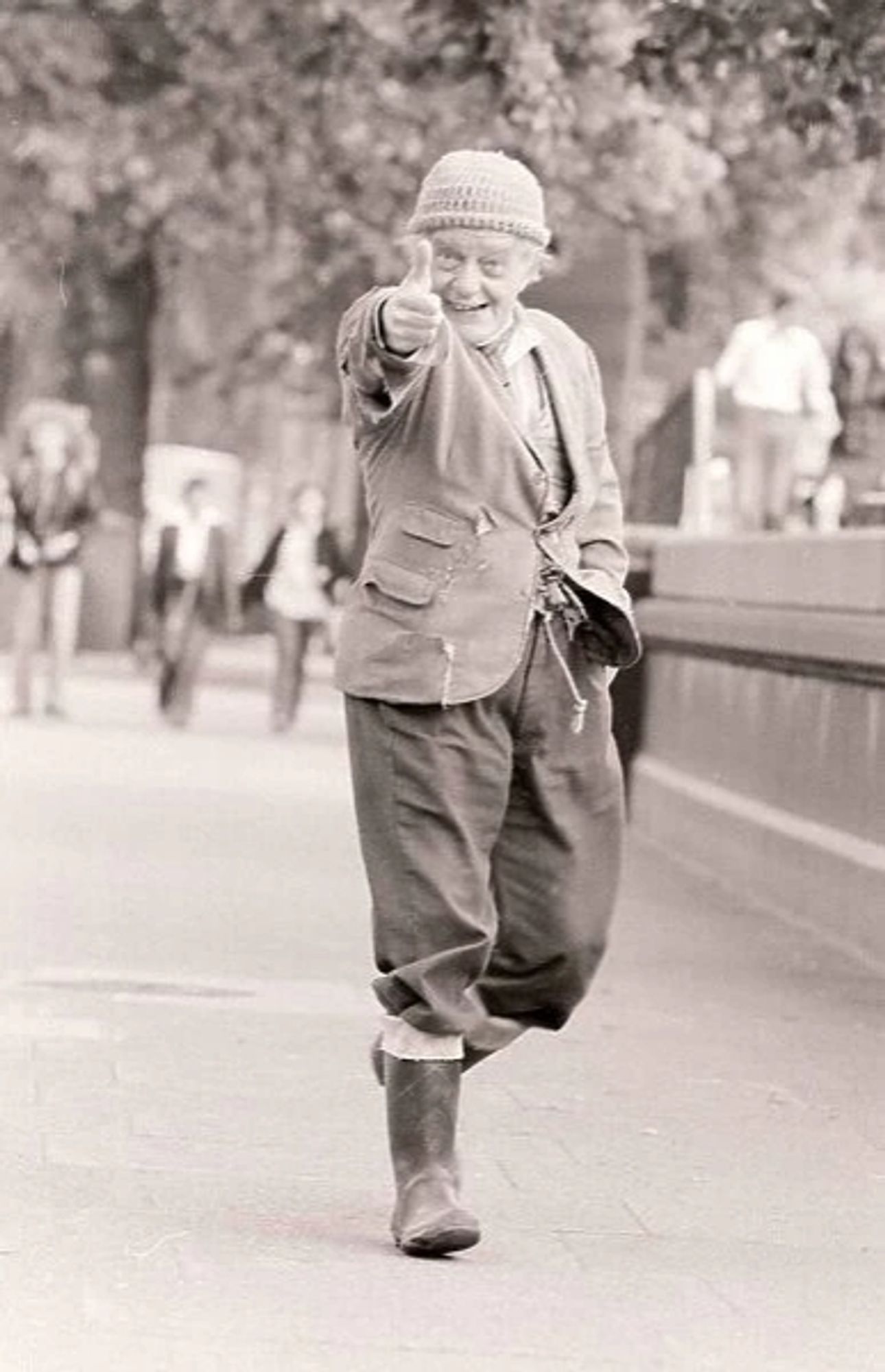 Compo from last of the summer wine, dressed in old beany, grimy tweed jacket, oversized trousers complete with jute string belt, tucked into mucky old wellies. Walking towards you, grinning inanely, right arm up and extended making thumbs up sign.