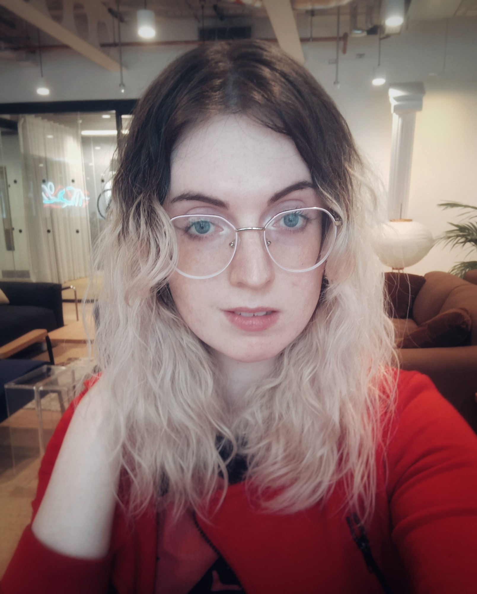 a selfie of me wearing a red hoodie and round glasses. I'm sat at work in a WeWork office