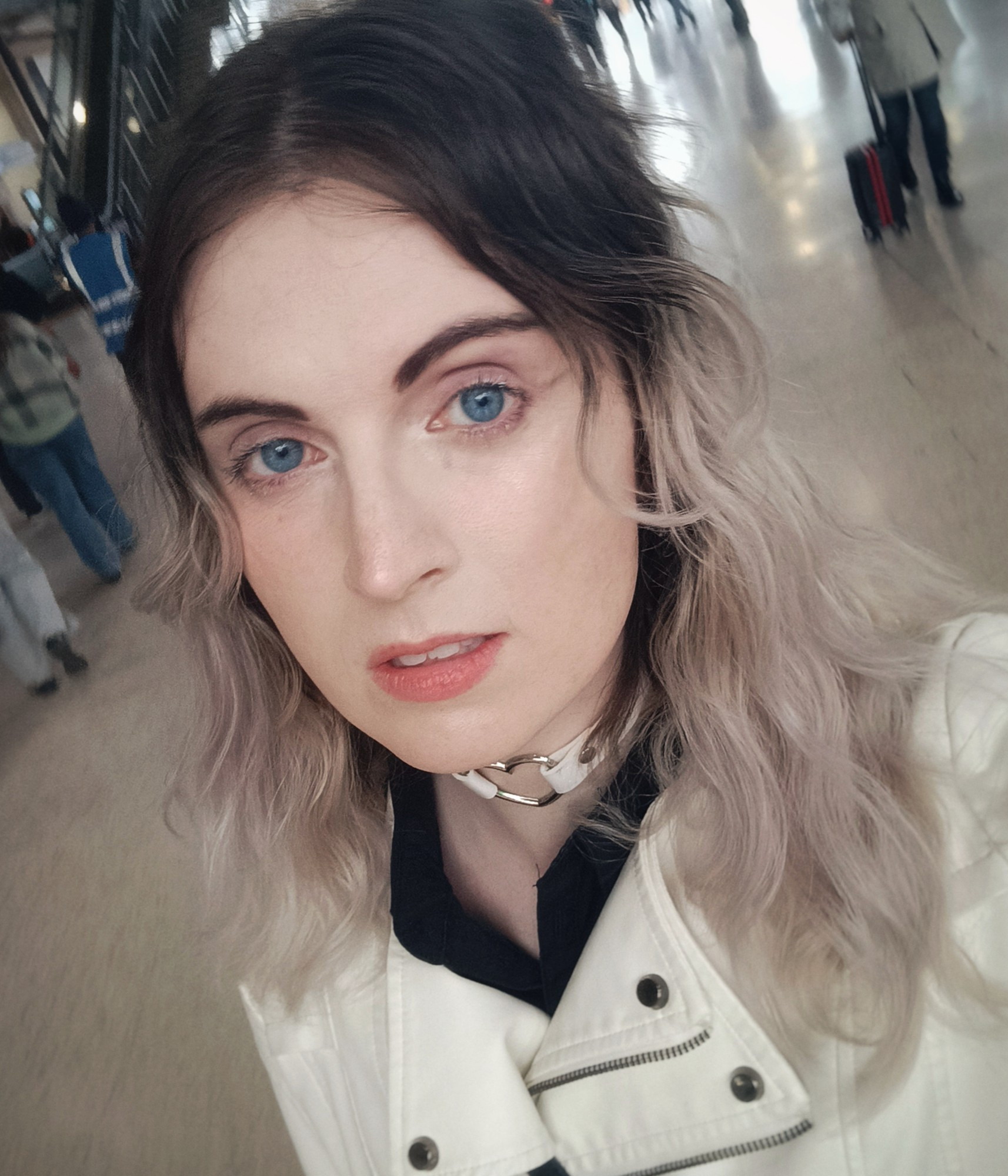 a selfie of me wearing a white choker and white jacket, I am not wearing glasses. I'm walking through a train station 