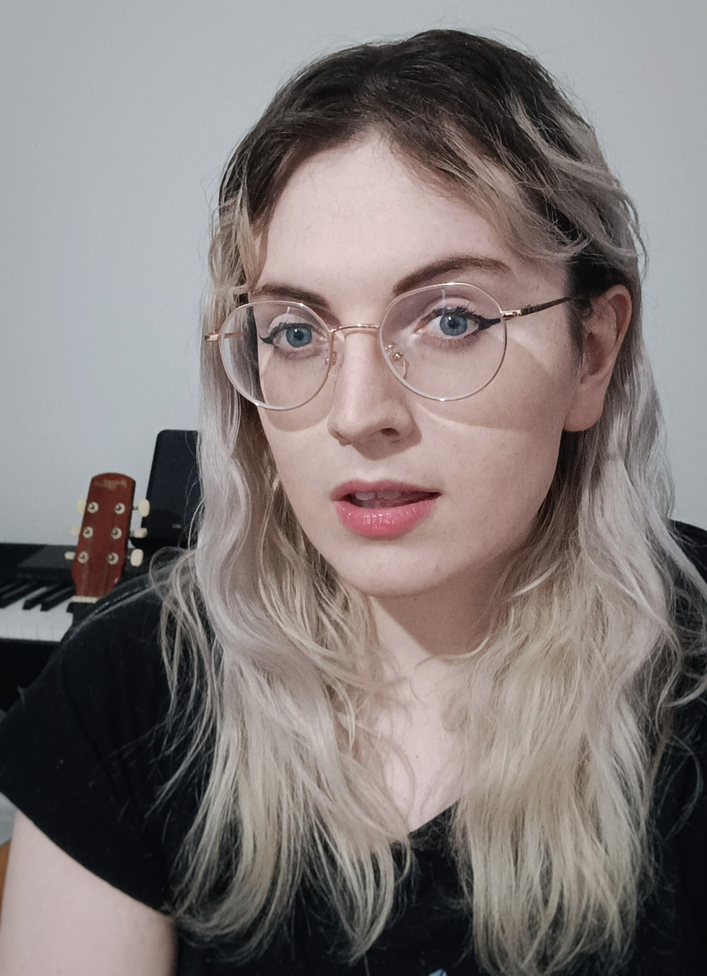 me sat in front of a piano and a guitar, my mouth is open slightly and I am wearing round glasses