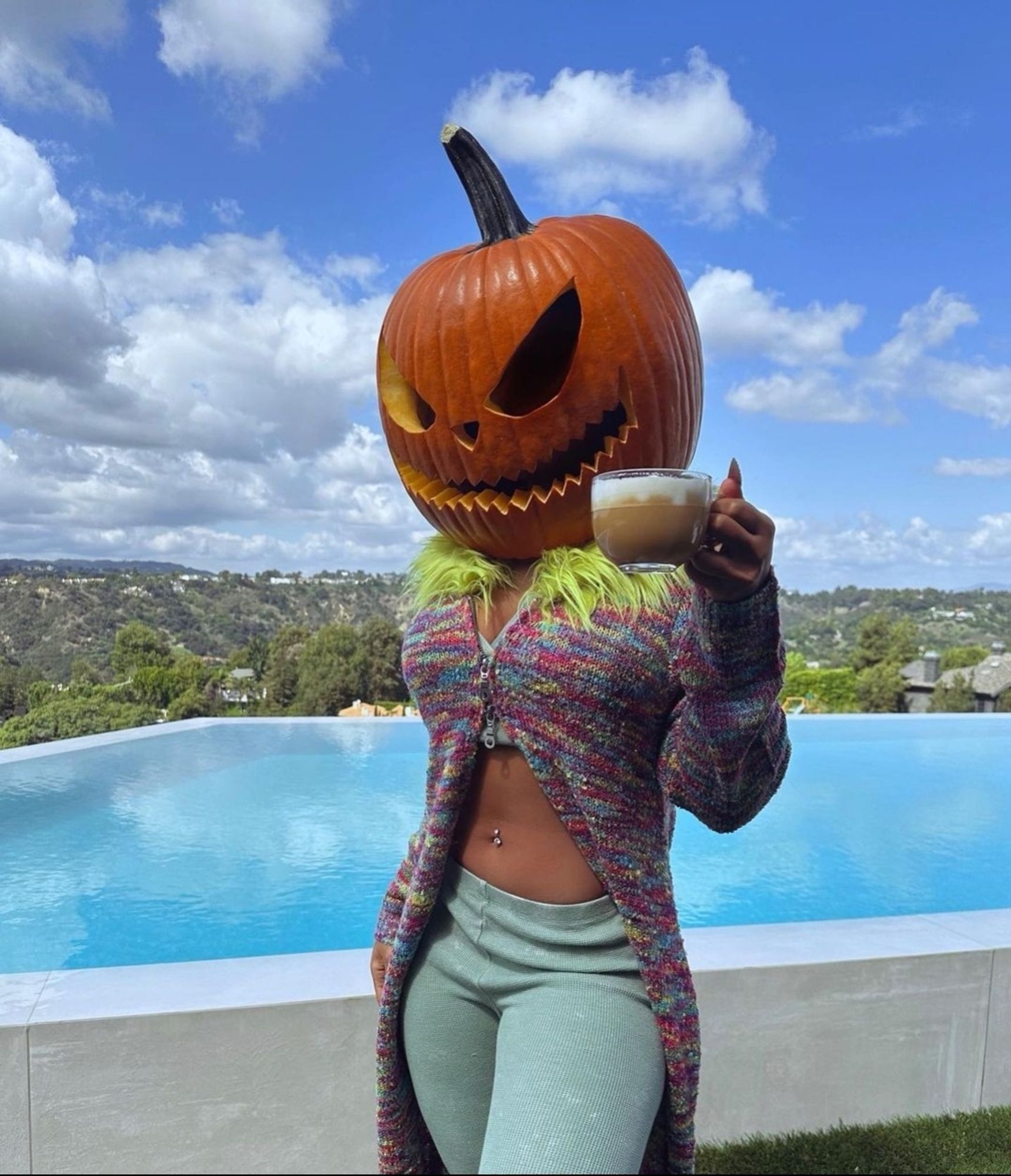 megan thee stallion wearing a carved pumpkin on her head while raising a cup of pumpkin spice latte