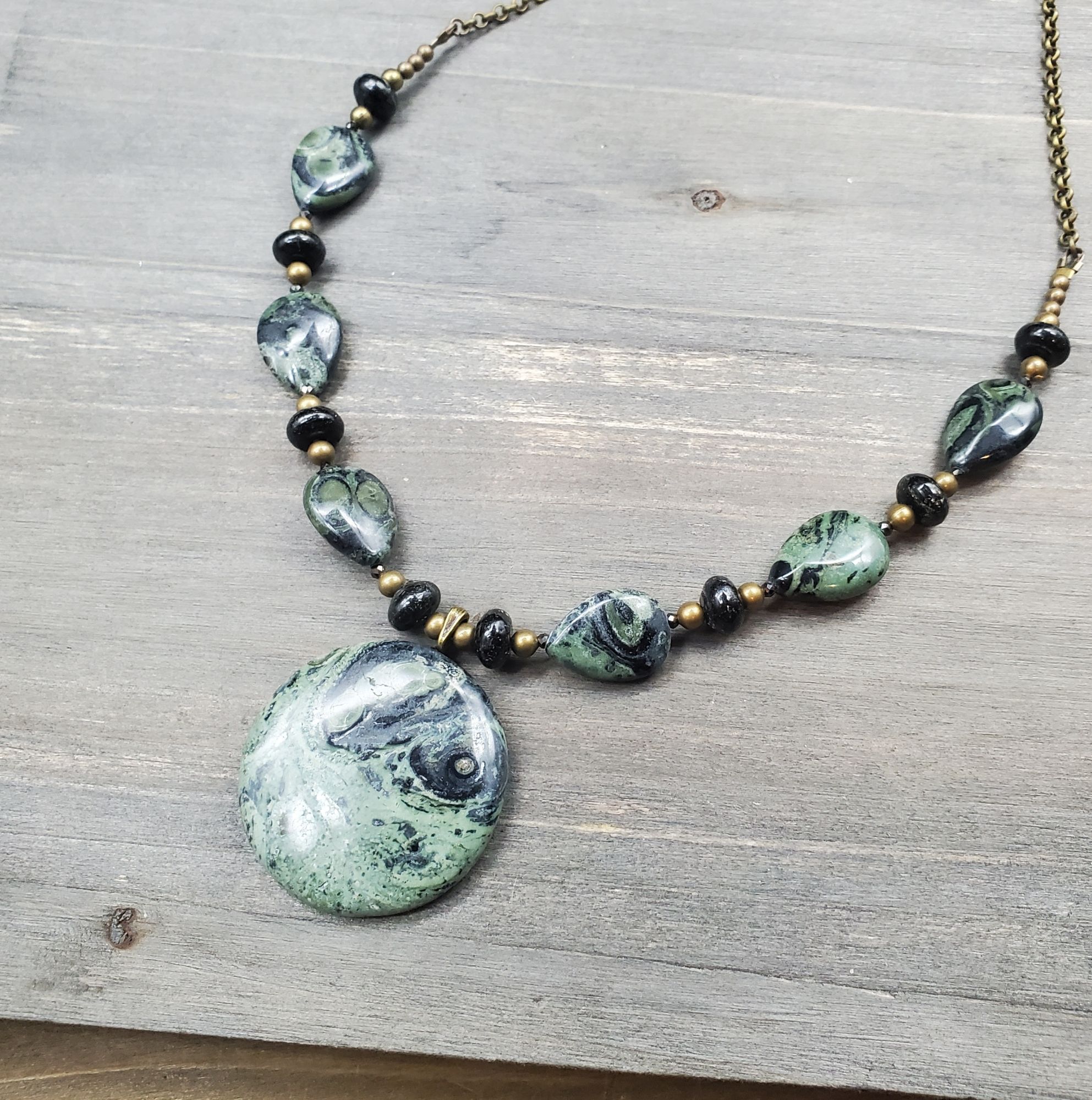 A bronze and jasper necklace in green and black with a round center stone and teardrop beads.