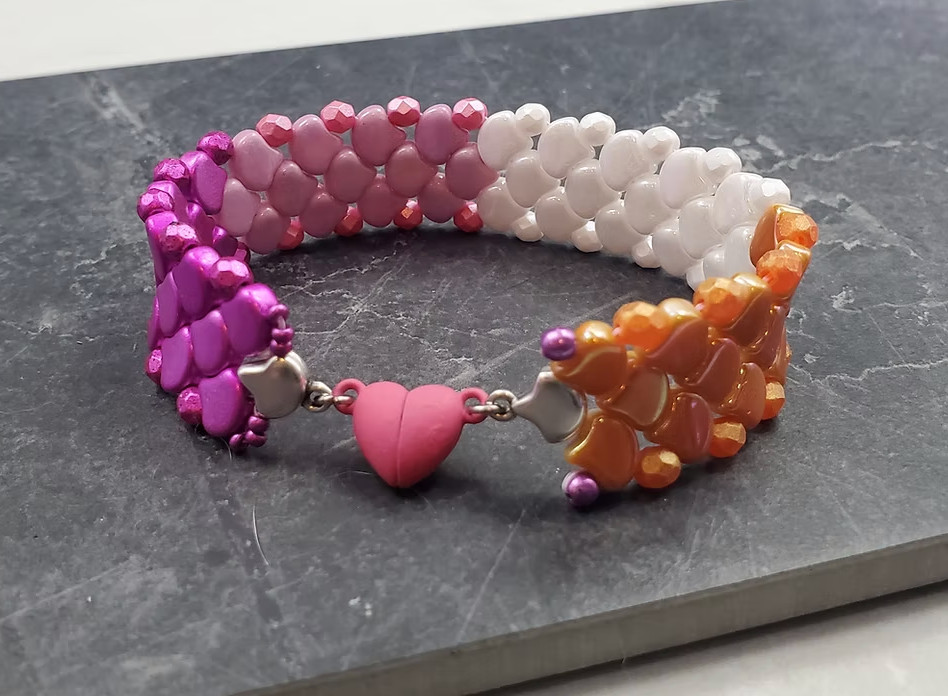 A lesbian flag colored sewn scale bead bracelet with a pink heart clasp 
