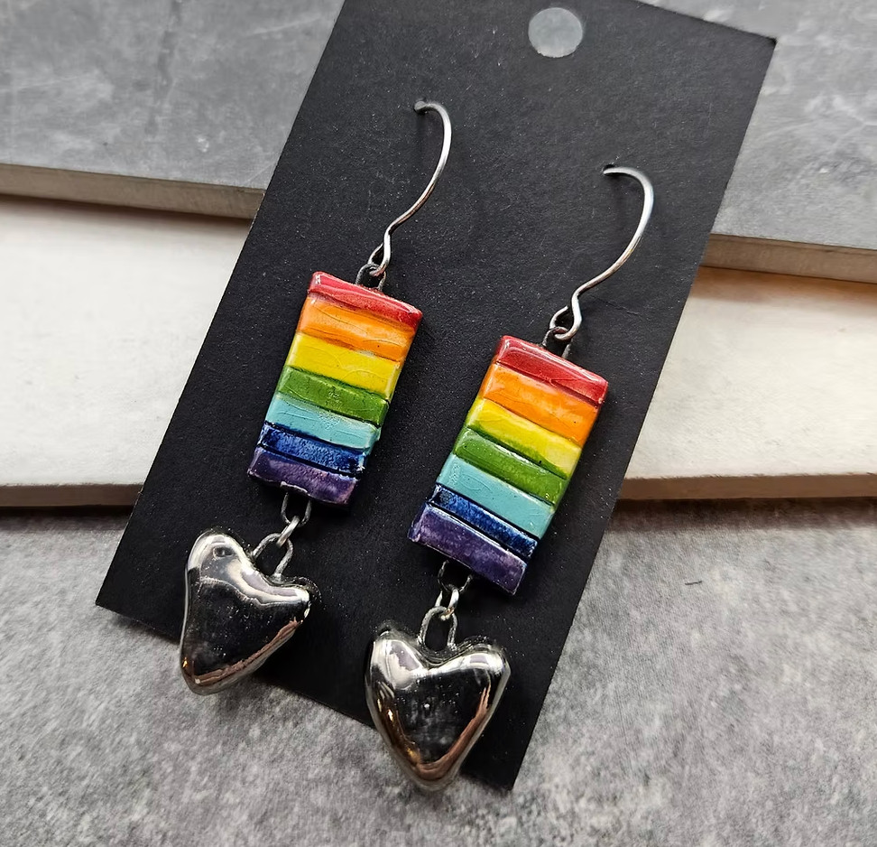 A pair of ceramic charm earrings with rainbow rectangles and silver/black hearts 