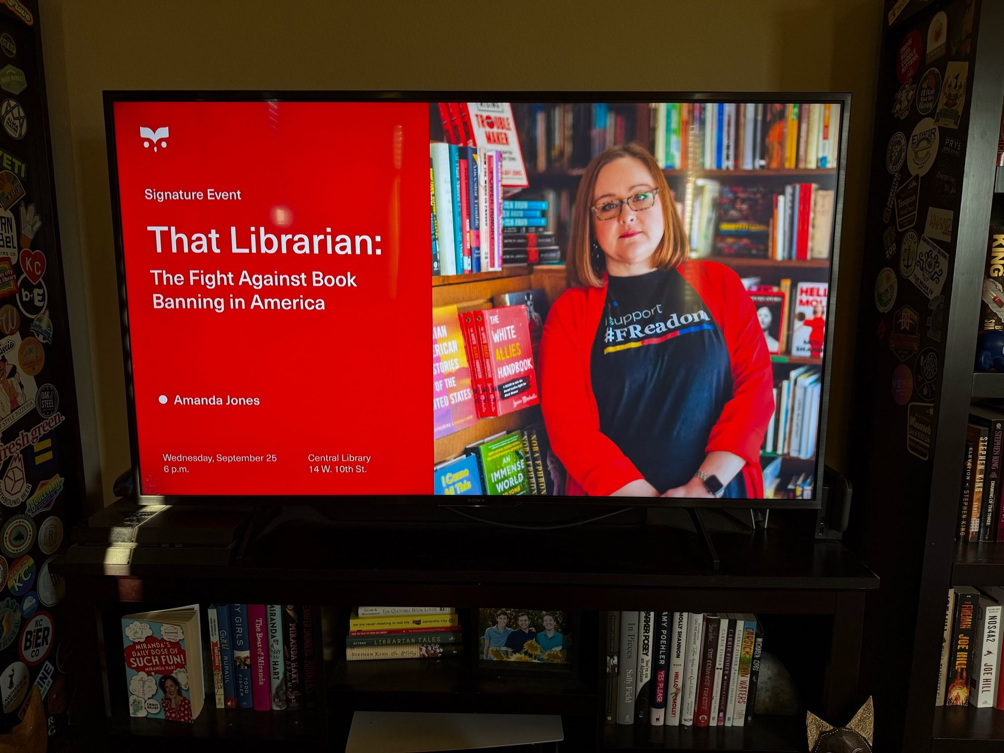 A large flat screen TV with the intro event slide that reads “That Librarian: The Fight Against Book Banning in America”