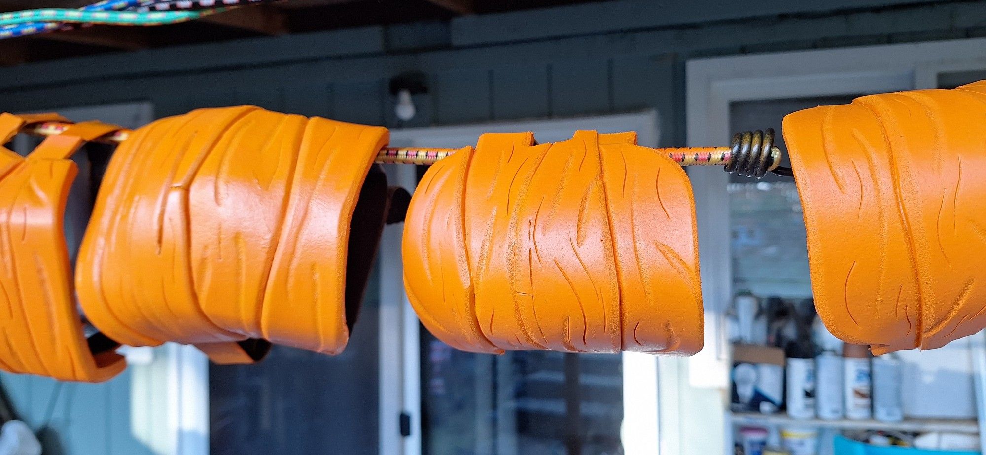 Wristbands, elbow pads, and kneepads along a line of bungee cords, the pumpkin orange paint drying in the sun