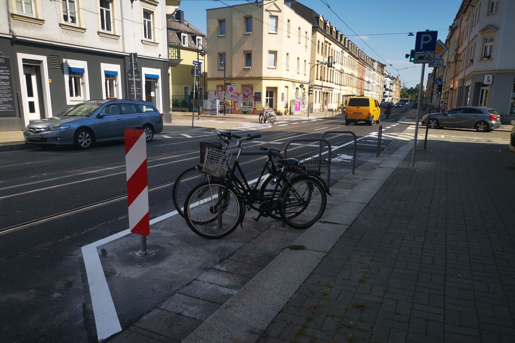 Blick auf eine Straßenkreuzung. Im Vordergrund wurde ein Bereich Abmarkiert und mit Fahrradbügeln bestückt. 