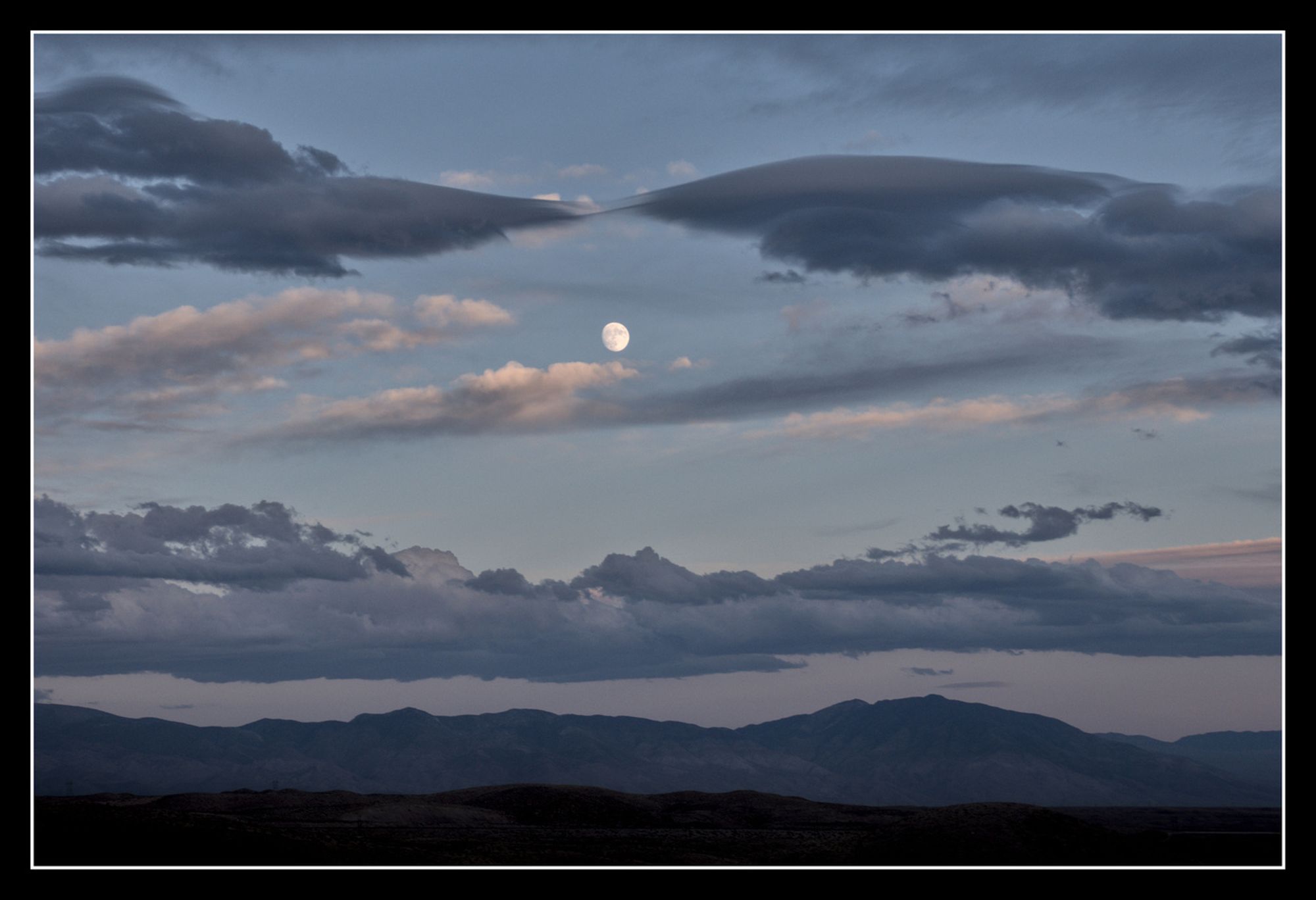 Moon over the White Mountains amidst scattered clouds at dusk.