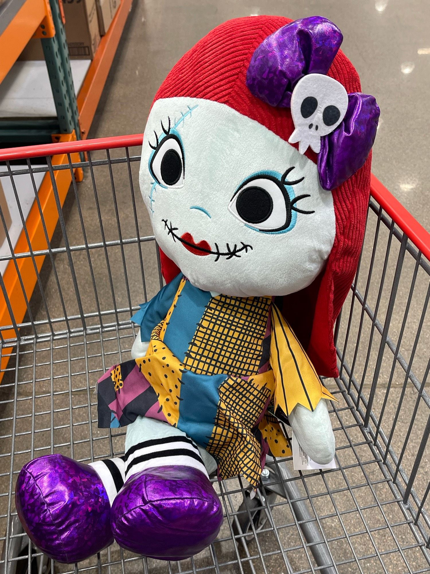 Sally from The Nightmare Before Christmas sitting cross legged in a Costco cart. She has a skeleton bow in her hair