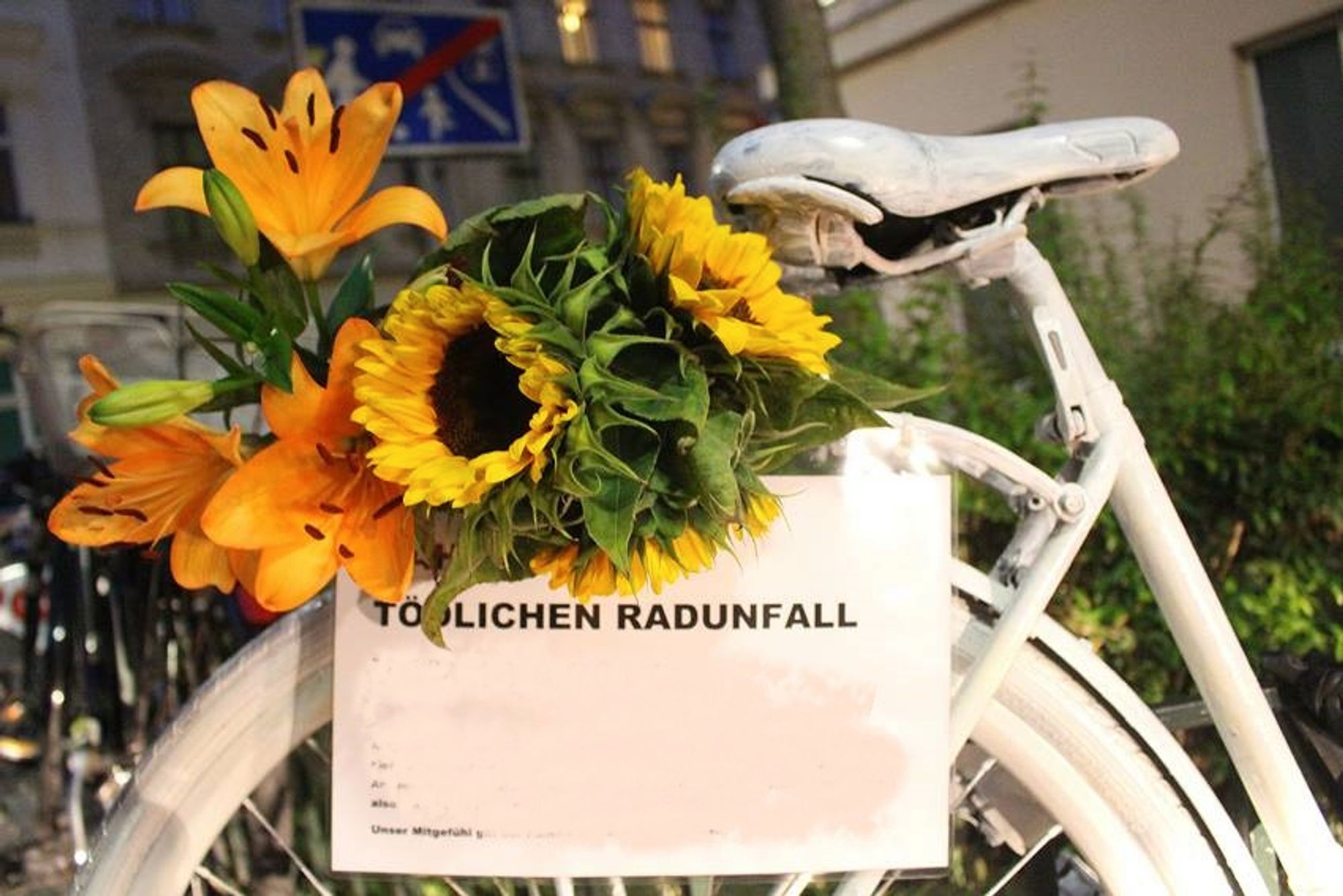 Ein mit gelben Blumen geschmücktes Ghostbike am Straßenrand.