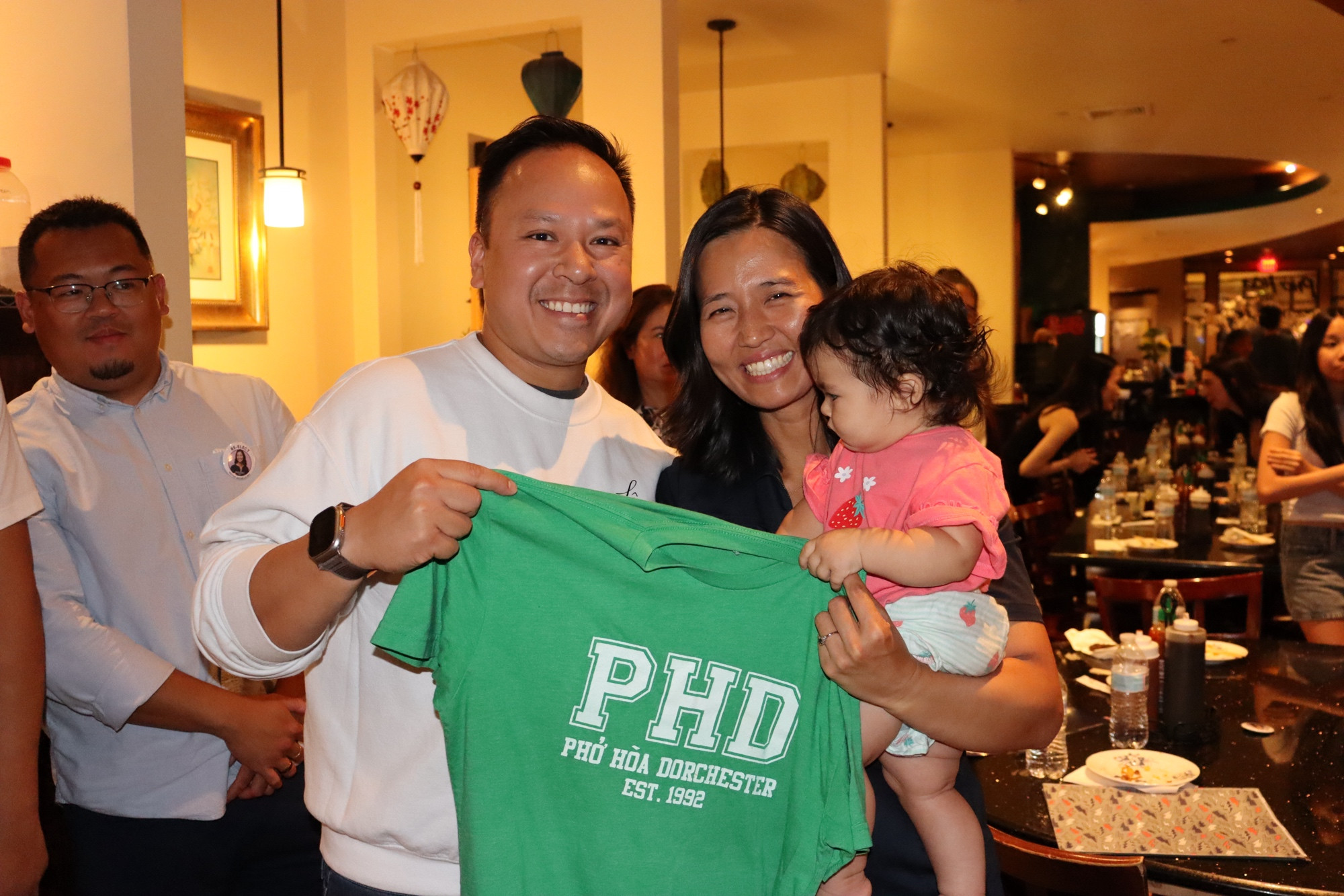 Tam Le holds a “PHD Pho Hoa Dorchester est. 1992” shirt with Mayor Wu and Mira 