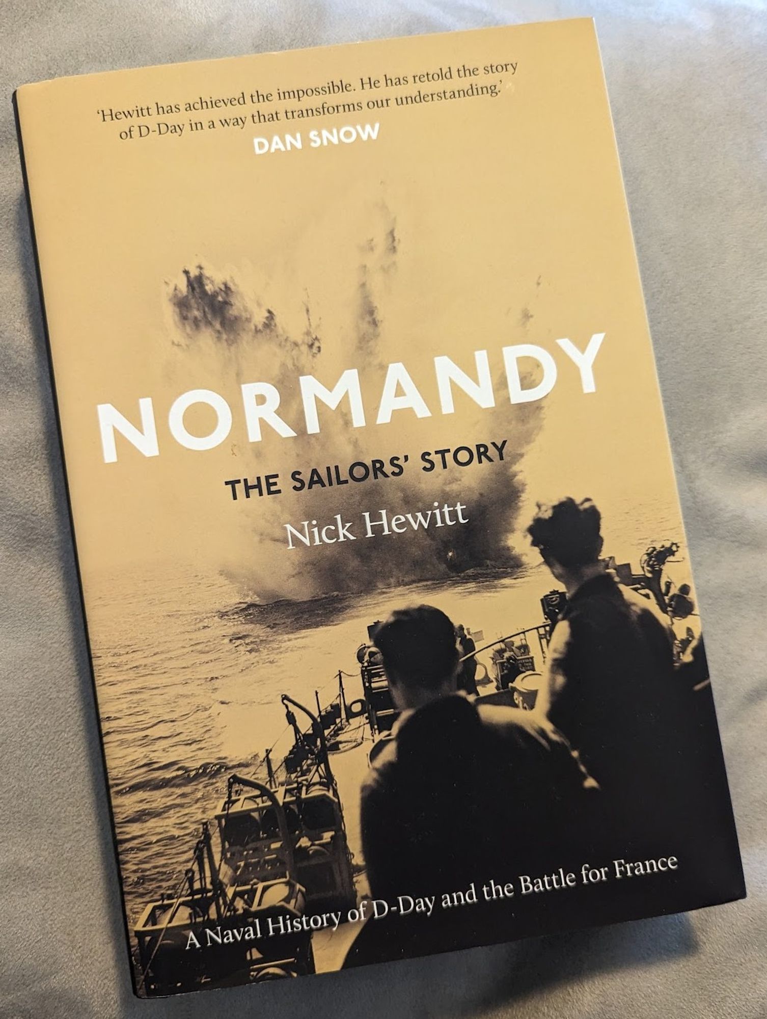 The front cover of the book "Normandy - The Sailor's Story" by Nick Hewitt, with a black and yellow (like black and white, but with yellow - not quite brown enough for sepia) photo of a depth charge exploding behind the stern of a ship.