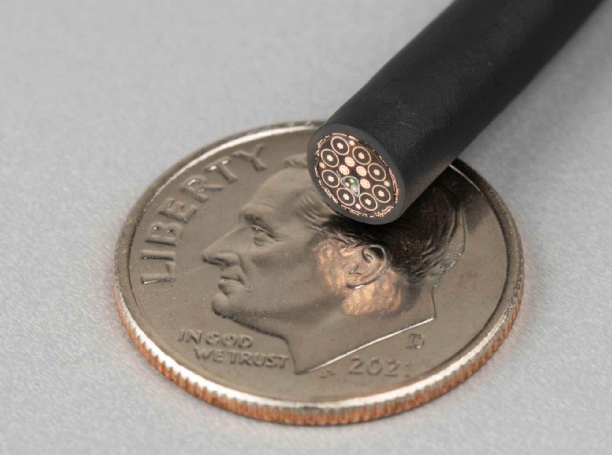 The cut end of a USB cable rests on a US dime, with all the wires inside visible.