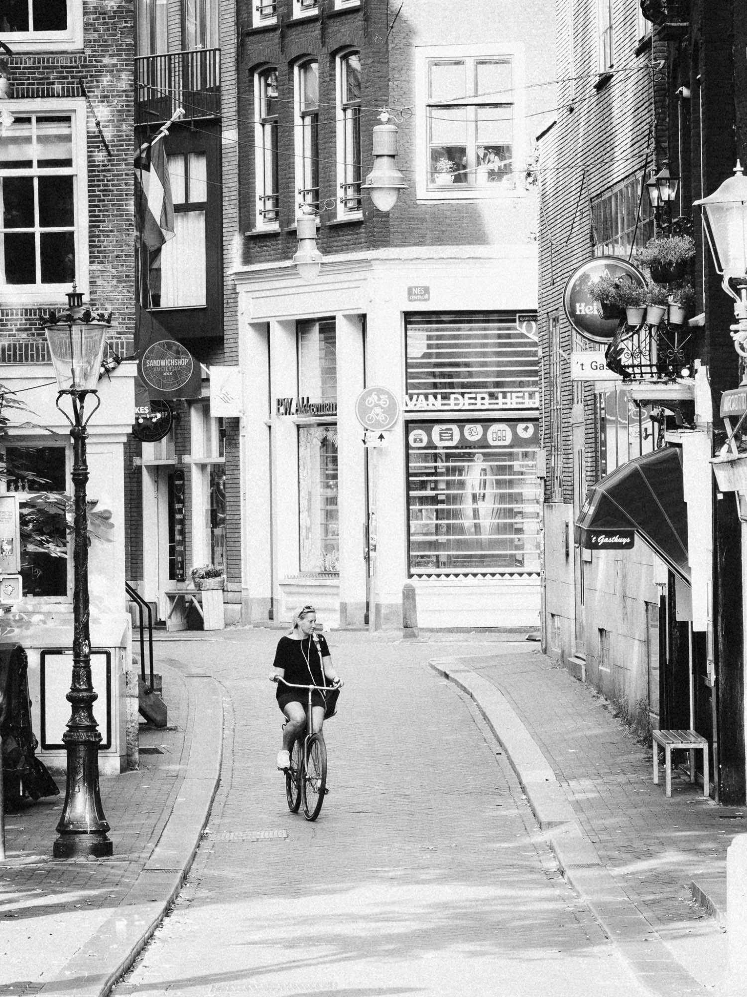 Black and white photo of a woman riding a bicycle on a quiet, narrow street in Amsterdam.