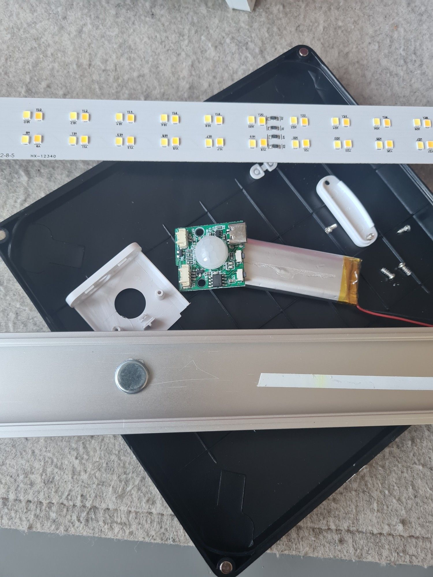 The results of me dismantling a cheap, broken, motion sensor light bar. It resulted in a tiny circuit board with a PIR sensor attached to it, an aluminium casing with magnets attached to it, the dead battery, a long board with SMD LEDs on it and  the rest of the plastic casing + screws