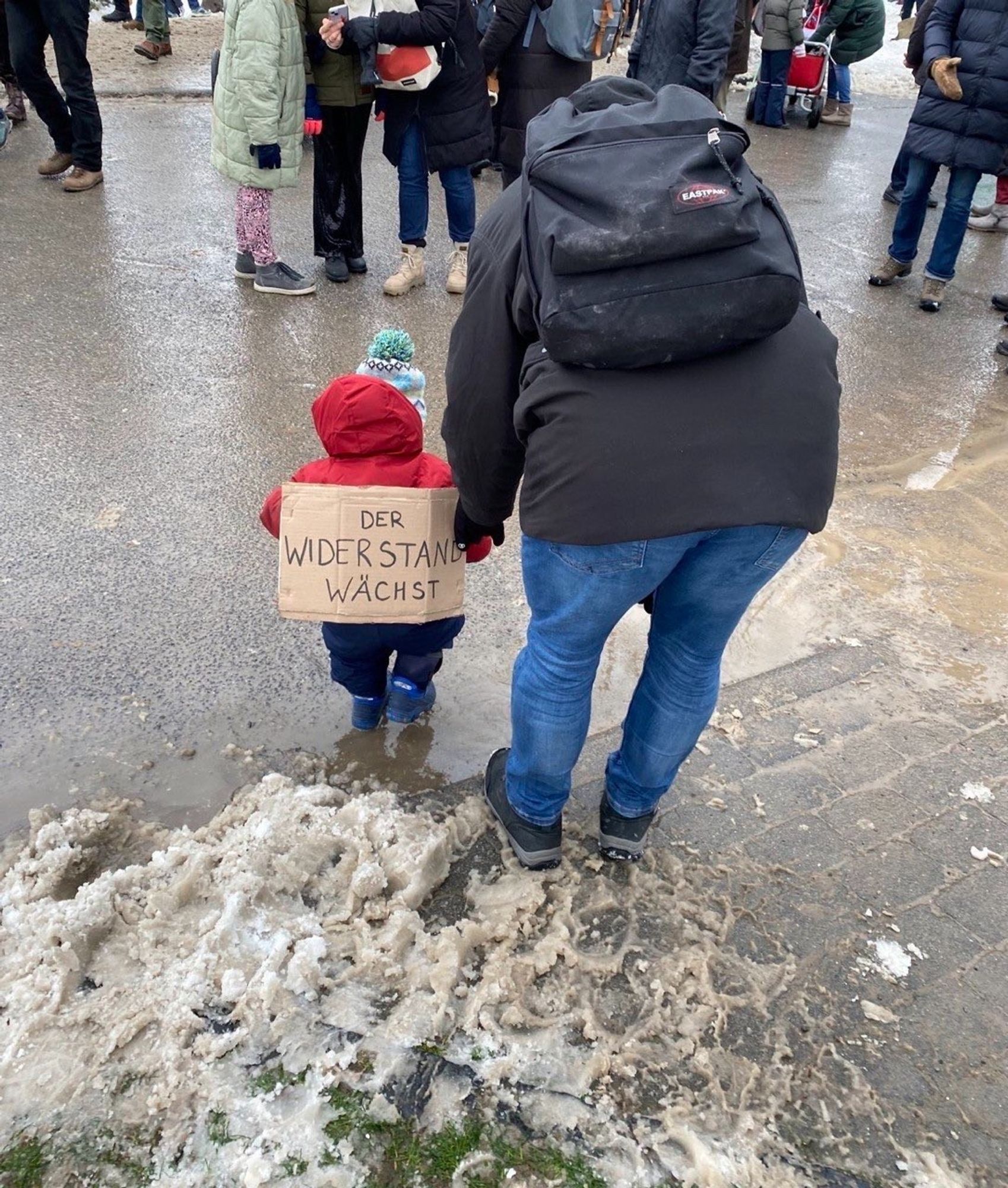 Köln- Demo: Nebeneinander zu Fuß auf der Straße Mutter und Kleinkind, auf dessen Rücken passendes kleines Schild: Der Widerstand wächst