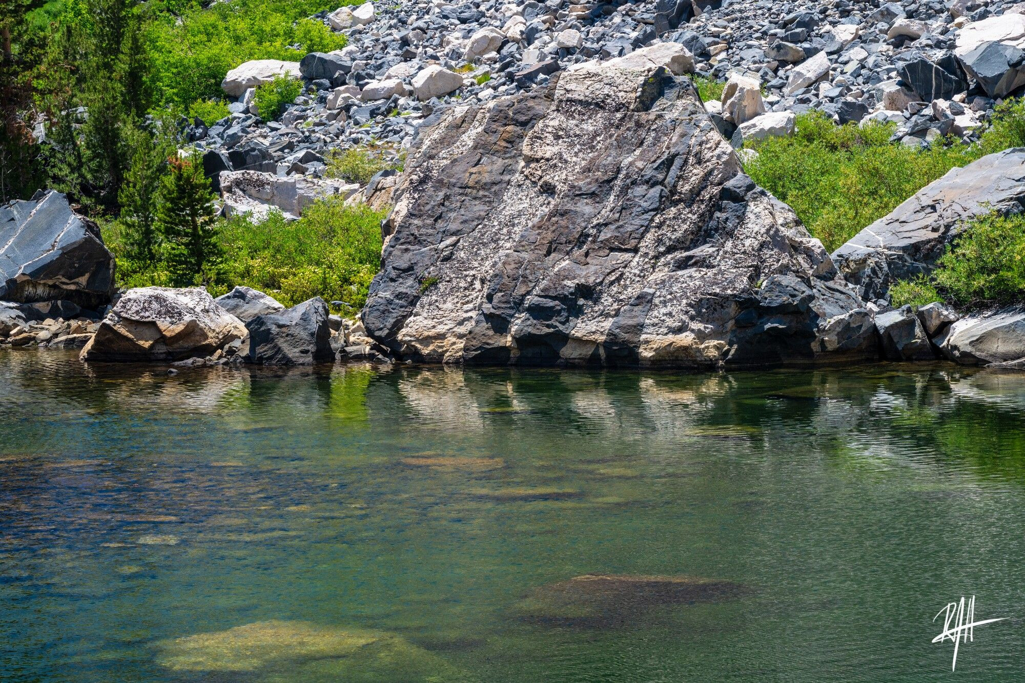 Massive chunk of gabbro (20'h x 40'w) with felsic intrusions sits in shallow turquoise lake shore, a remnant rockfall. 