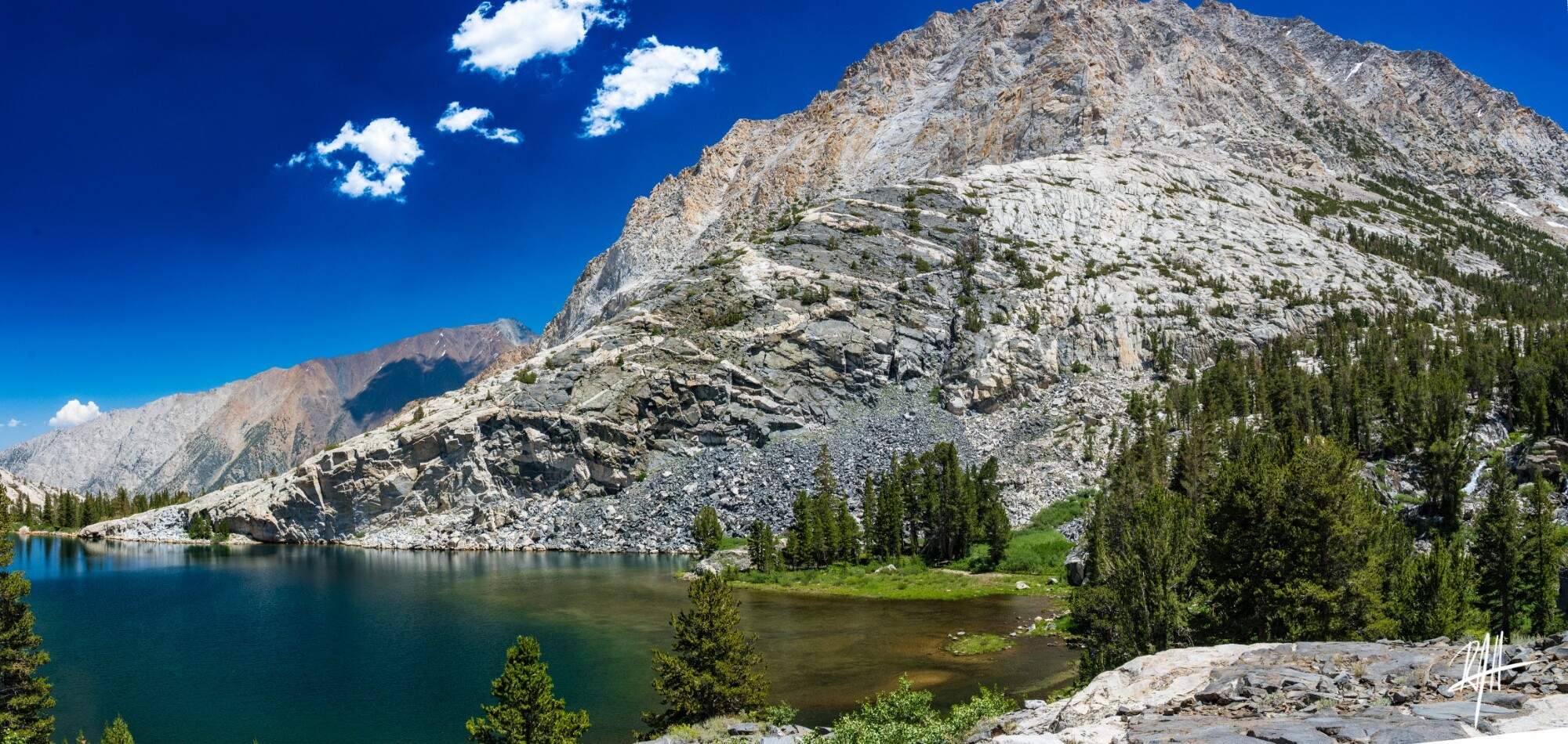 Panorama stitched looking to east from West shore of Pine Lake. darker gabbro rocks intruded by felsic rocks that make up the mountain on the right. 