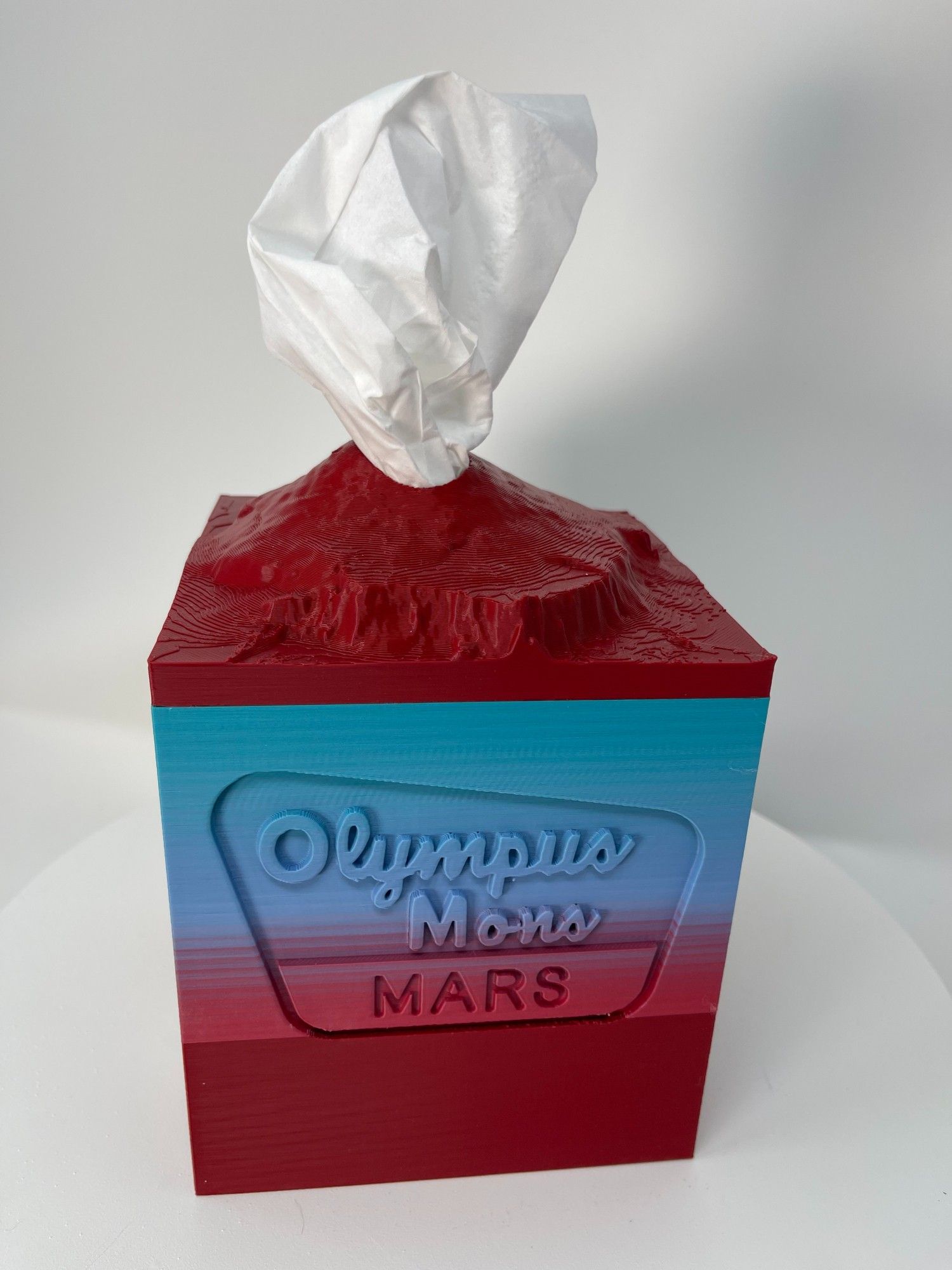 Cubic tissue box cover in the shape of Olympus Mons in red and blue gradient.